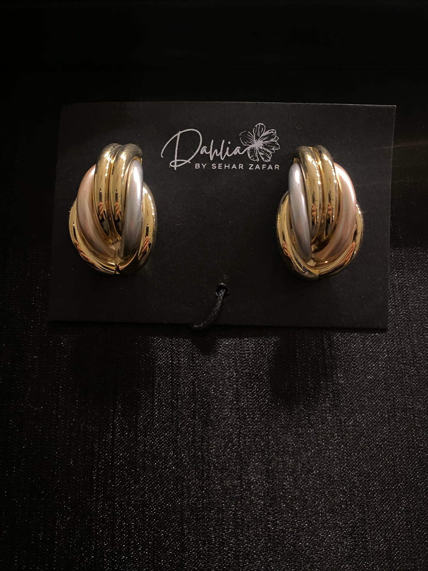 Gold, silver, and rose gold interlinked loop earrings on black branded card
