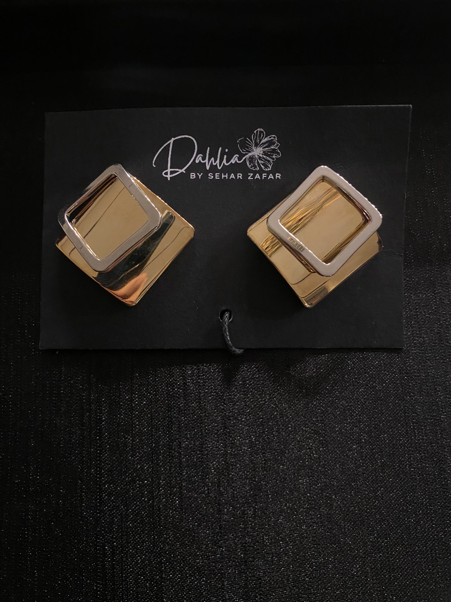 Gold and silver layered square earrings on black branded card