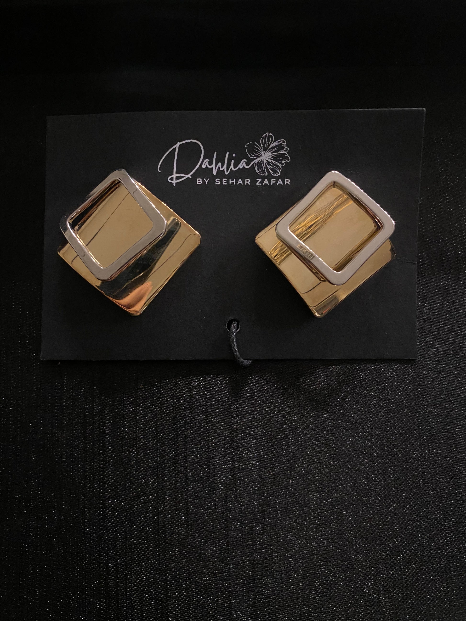 Gold and silver layered square earrings on black branded card