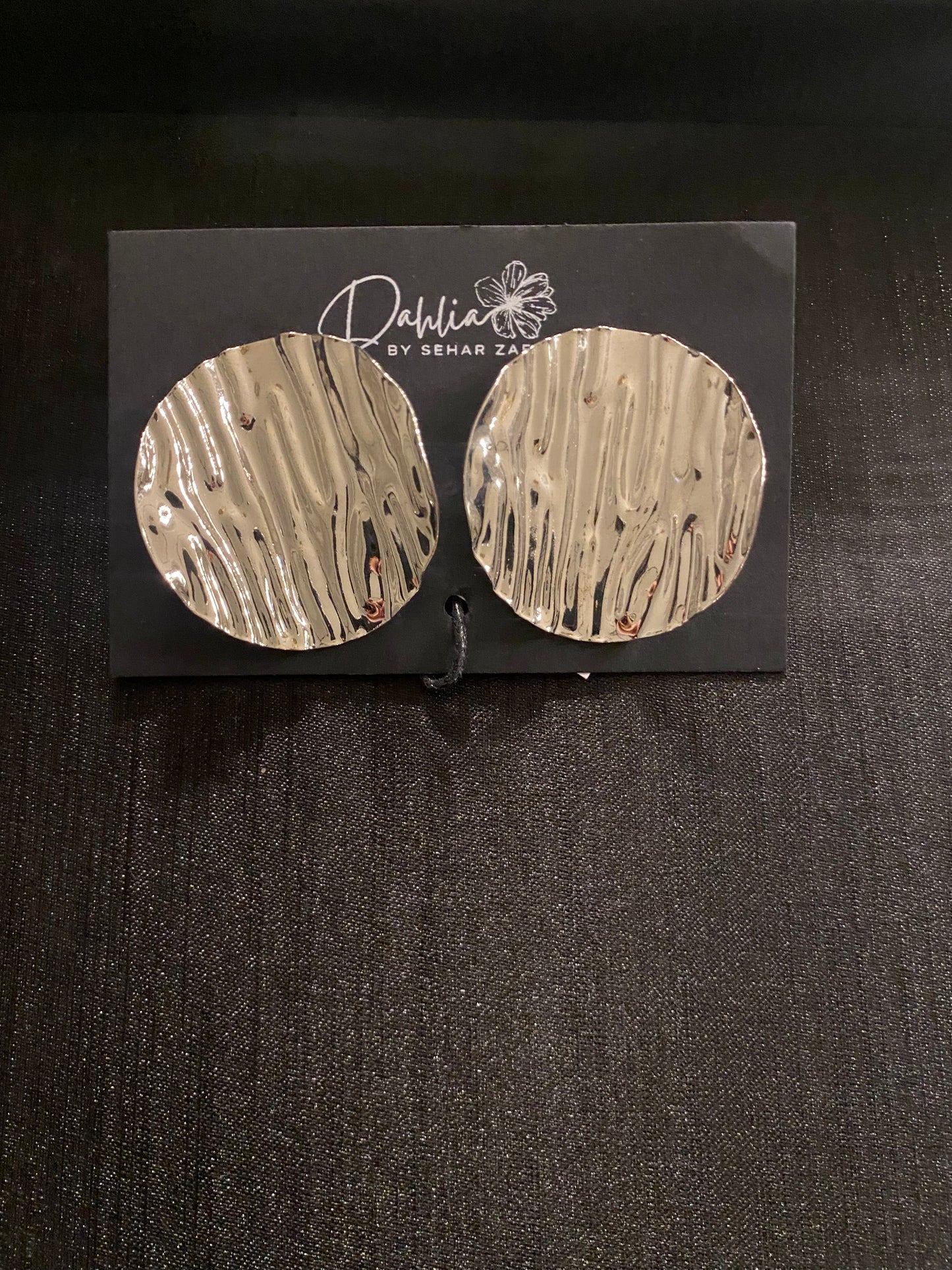 Large round gold earrings with wavy texture on black branded card