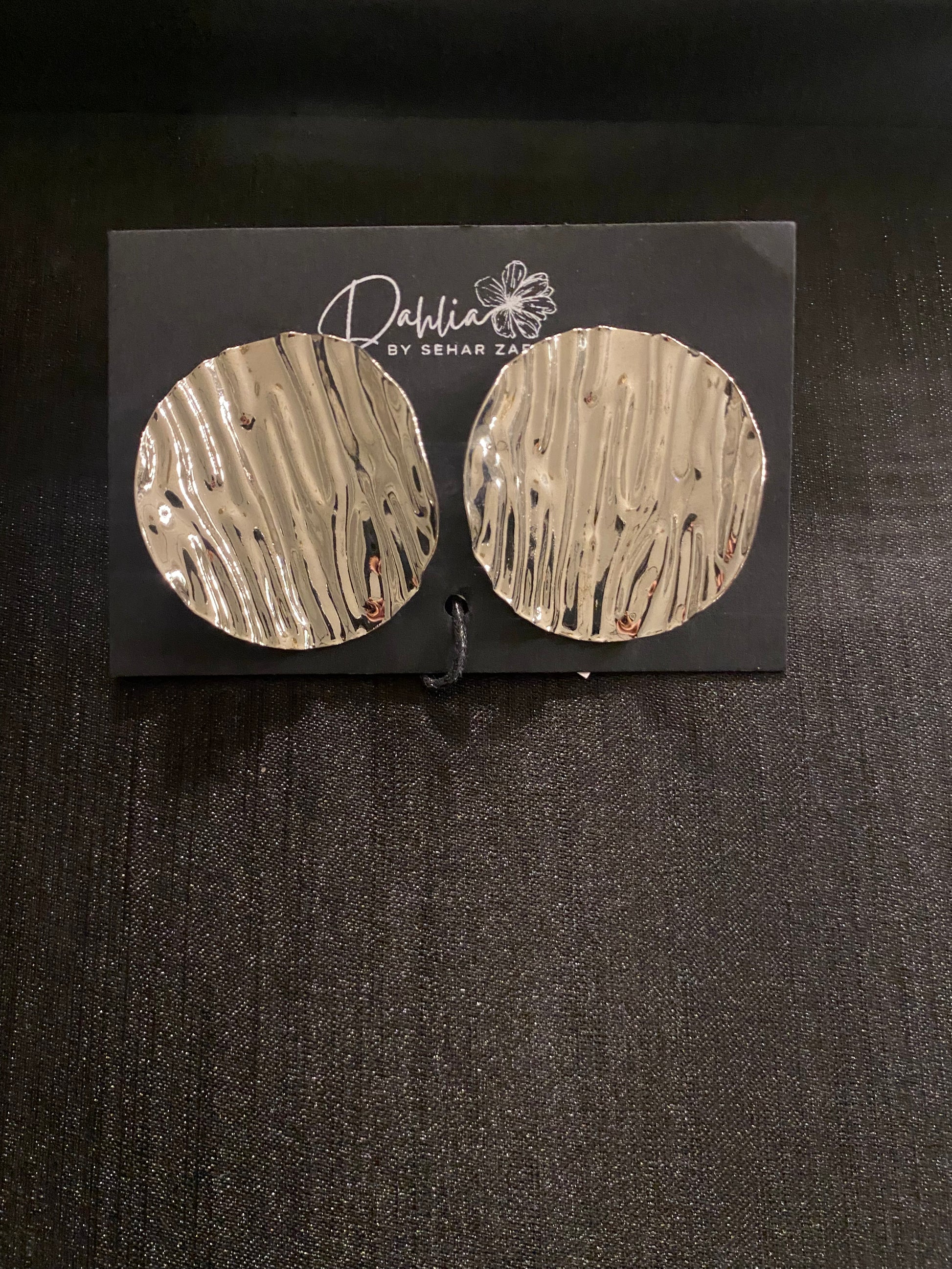 Large round gold earrings with wavy texture on black branded card