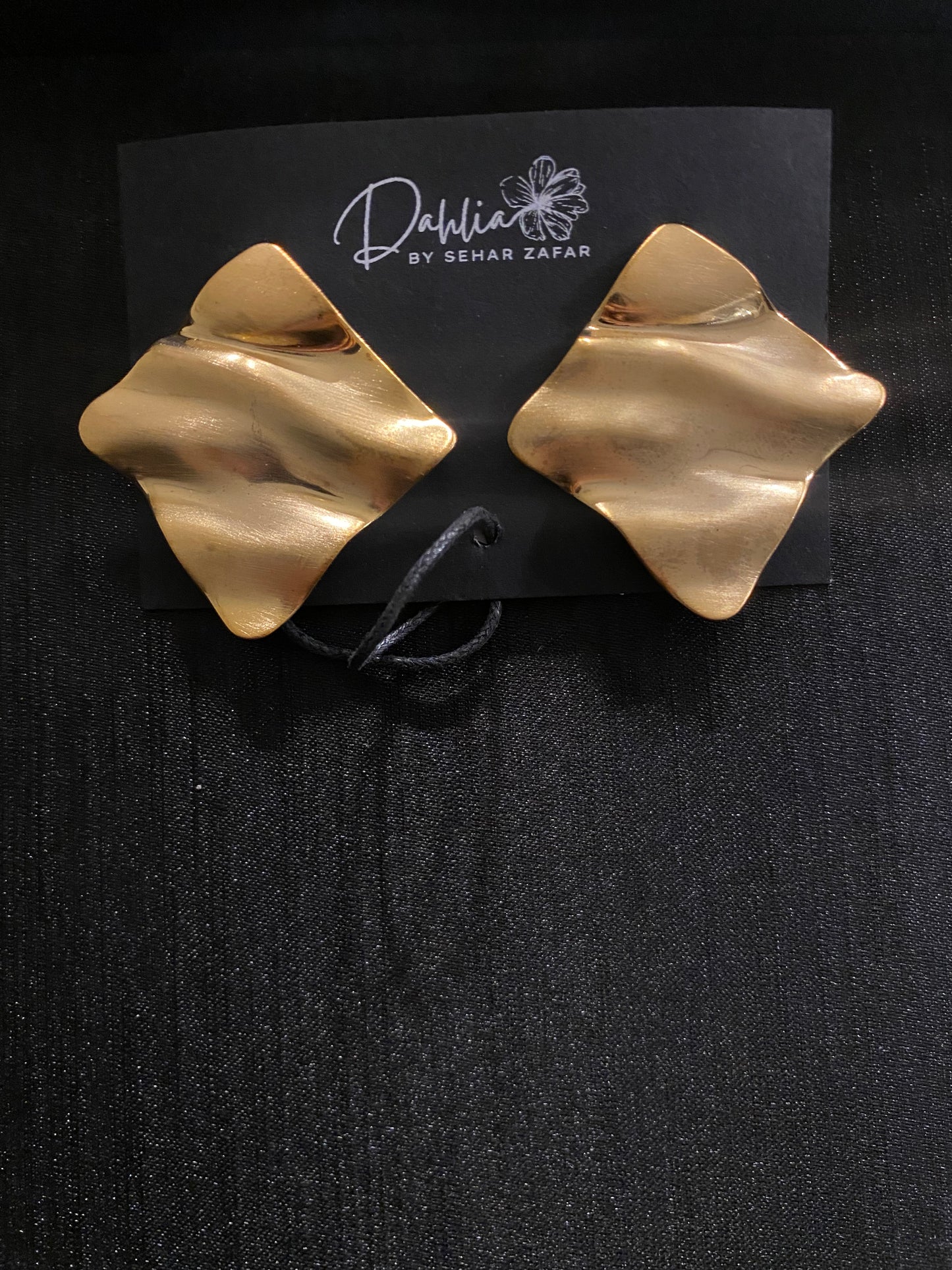 Gold abstract square earrings with wavy texture on black branded card