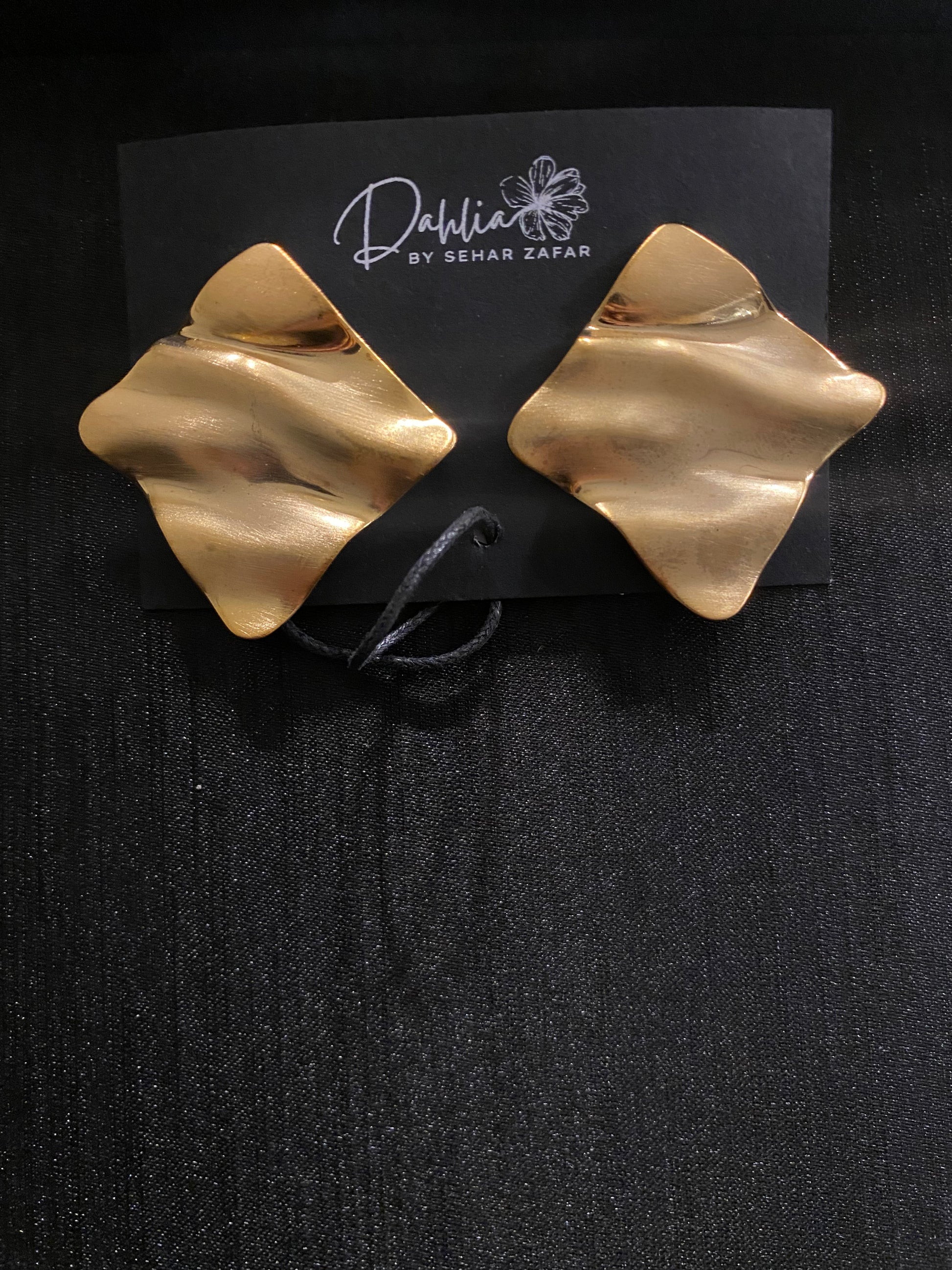 Gold abstract square earrings with wavy texture on black branded card