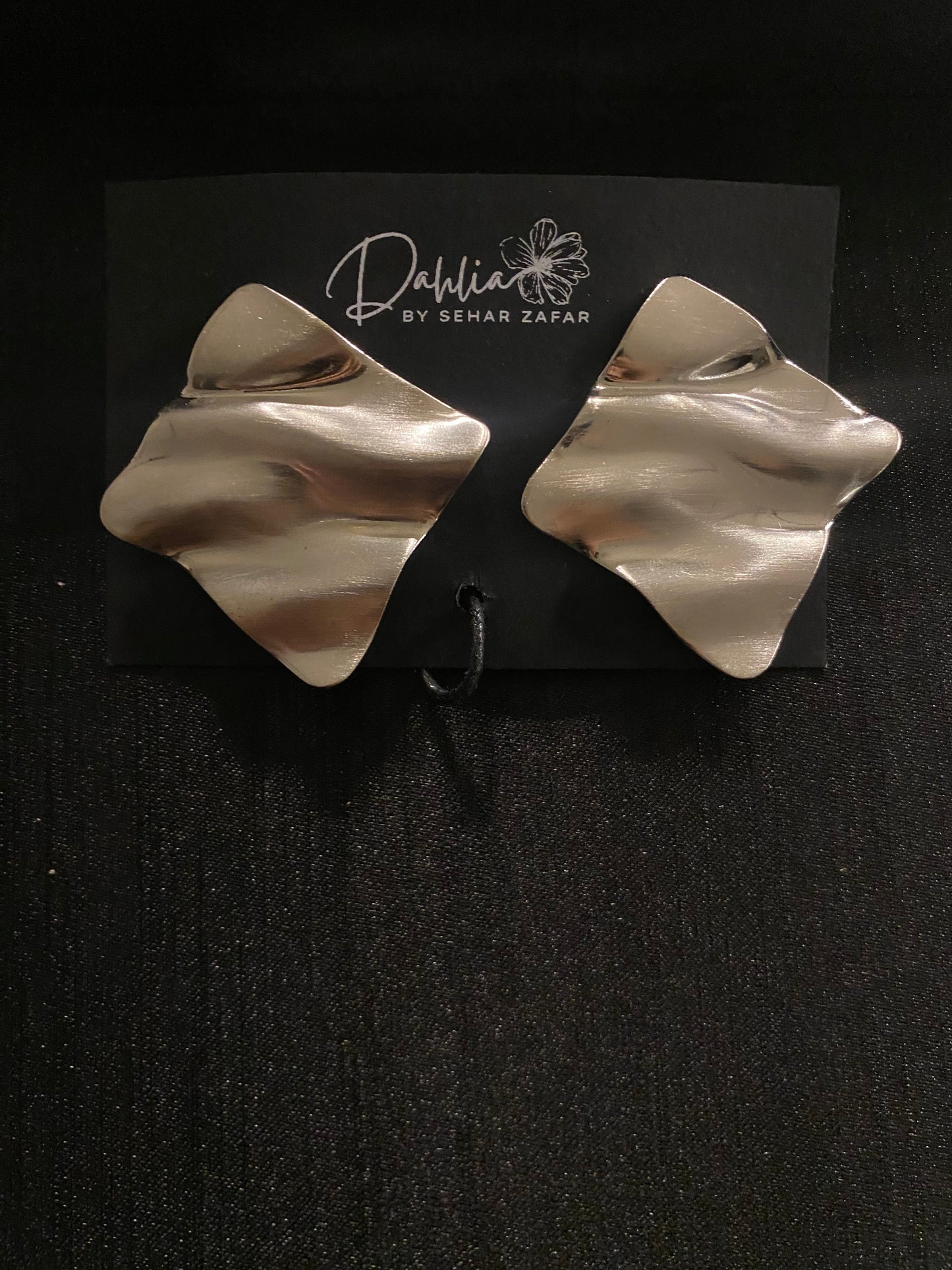 Gold abstract square earrings with wavy texture on black branded card