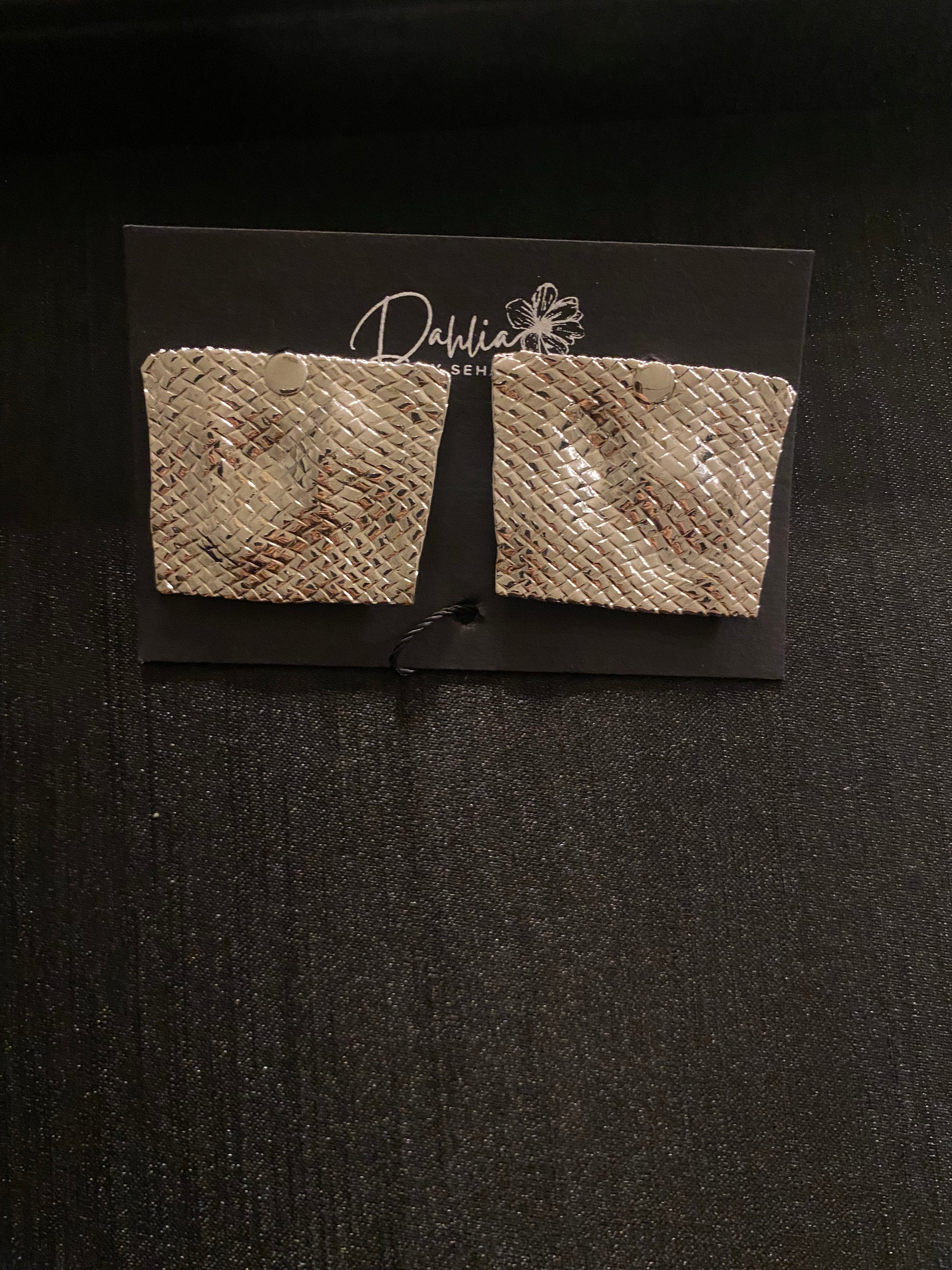 Gold square earrings with woven texture and curved shape on black branded card