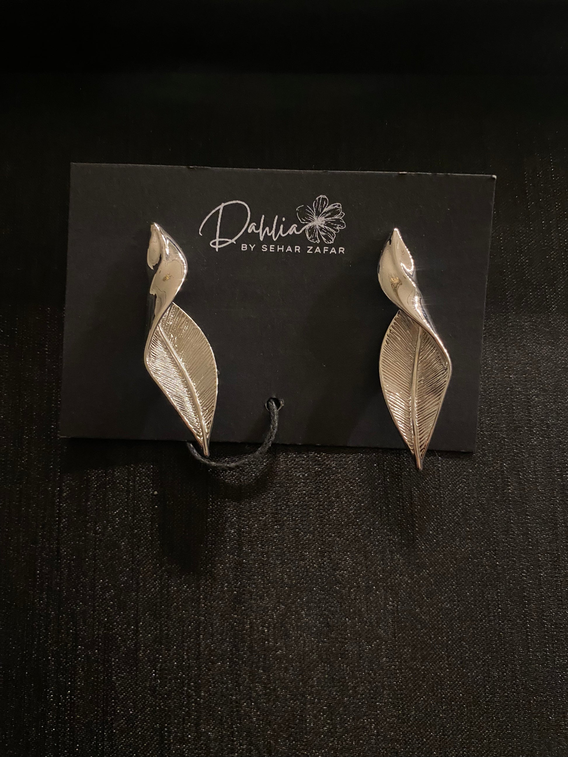 Silver leaf-shaped earrings with vein and petal detail on black branded card