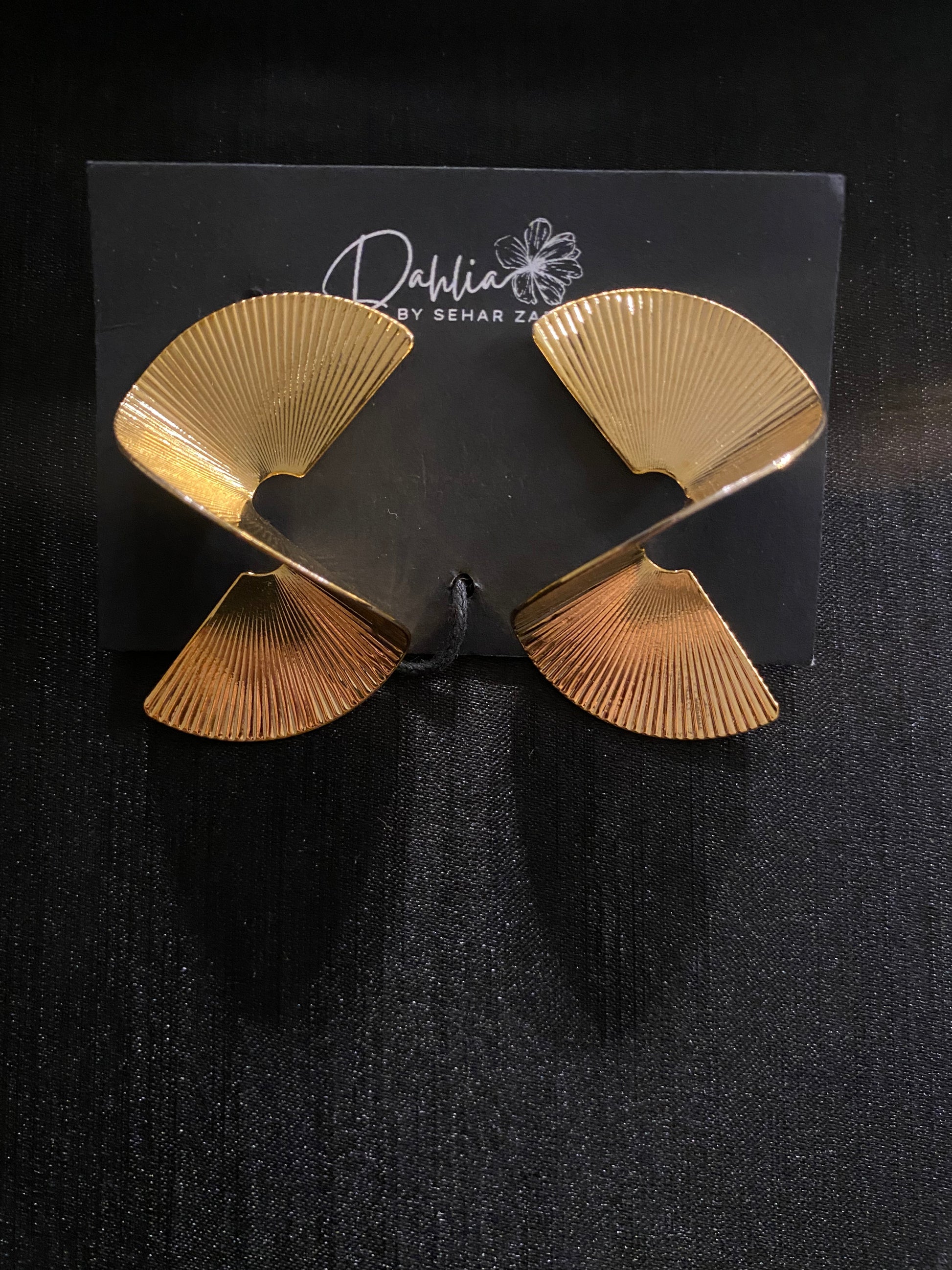 Fan-shaped metallic earrings with ridged texture on black branded card