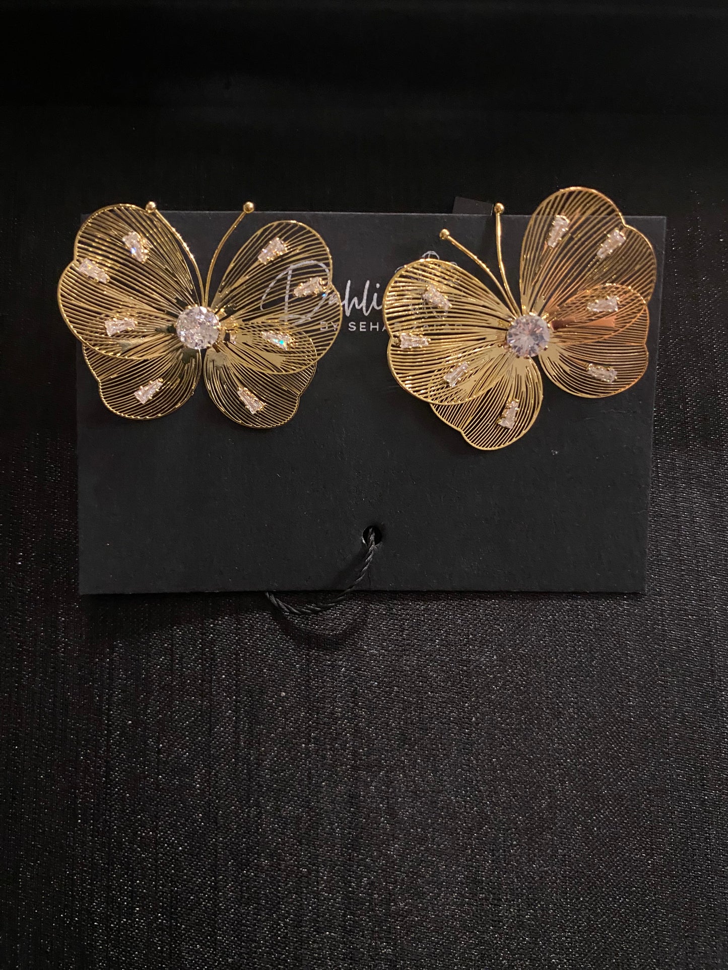 Gold wire butterfly earrings with gemstone wings on black branded card