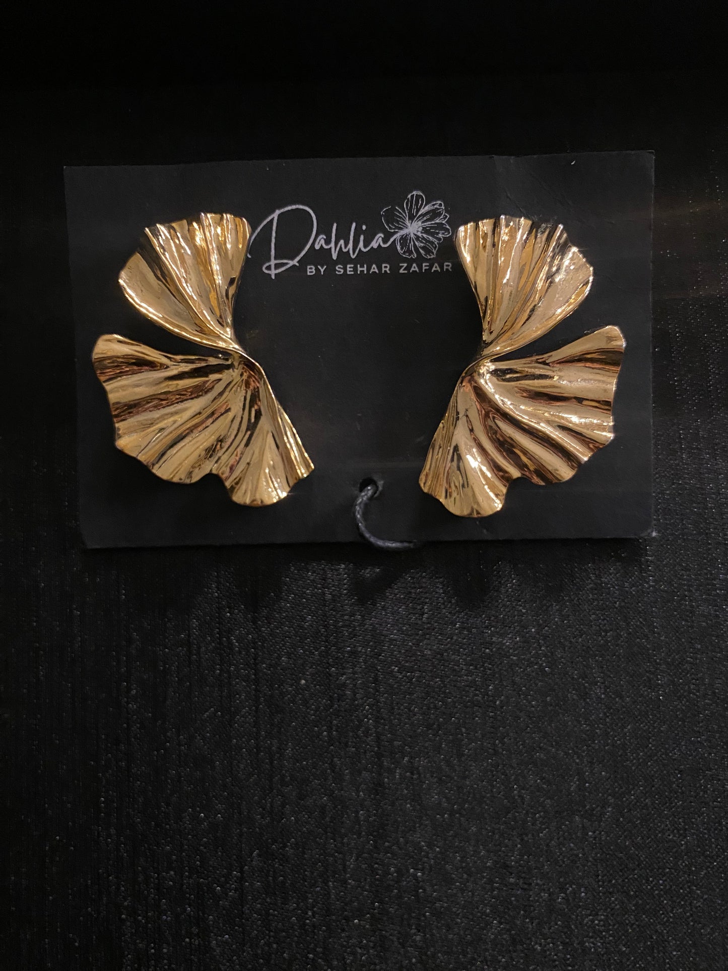 Gold sculptural earrings with pleated leaf-like design on black branded card
