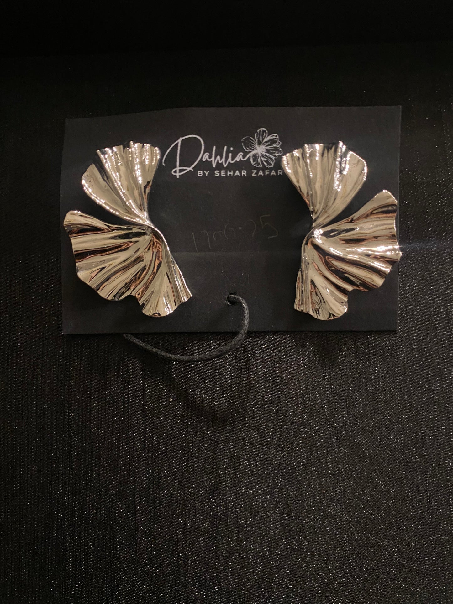 Gold sculptural earrings with pleated leaf-like design on black branded card