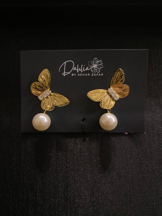 Gold butterfly earrings with gemstone body and pearl drop on black branded card