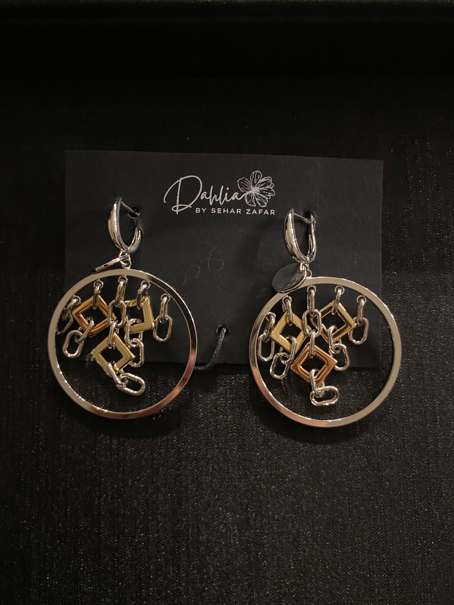 Gold circular earrings with geometric hanging elements in mixed metal on black branded card
