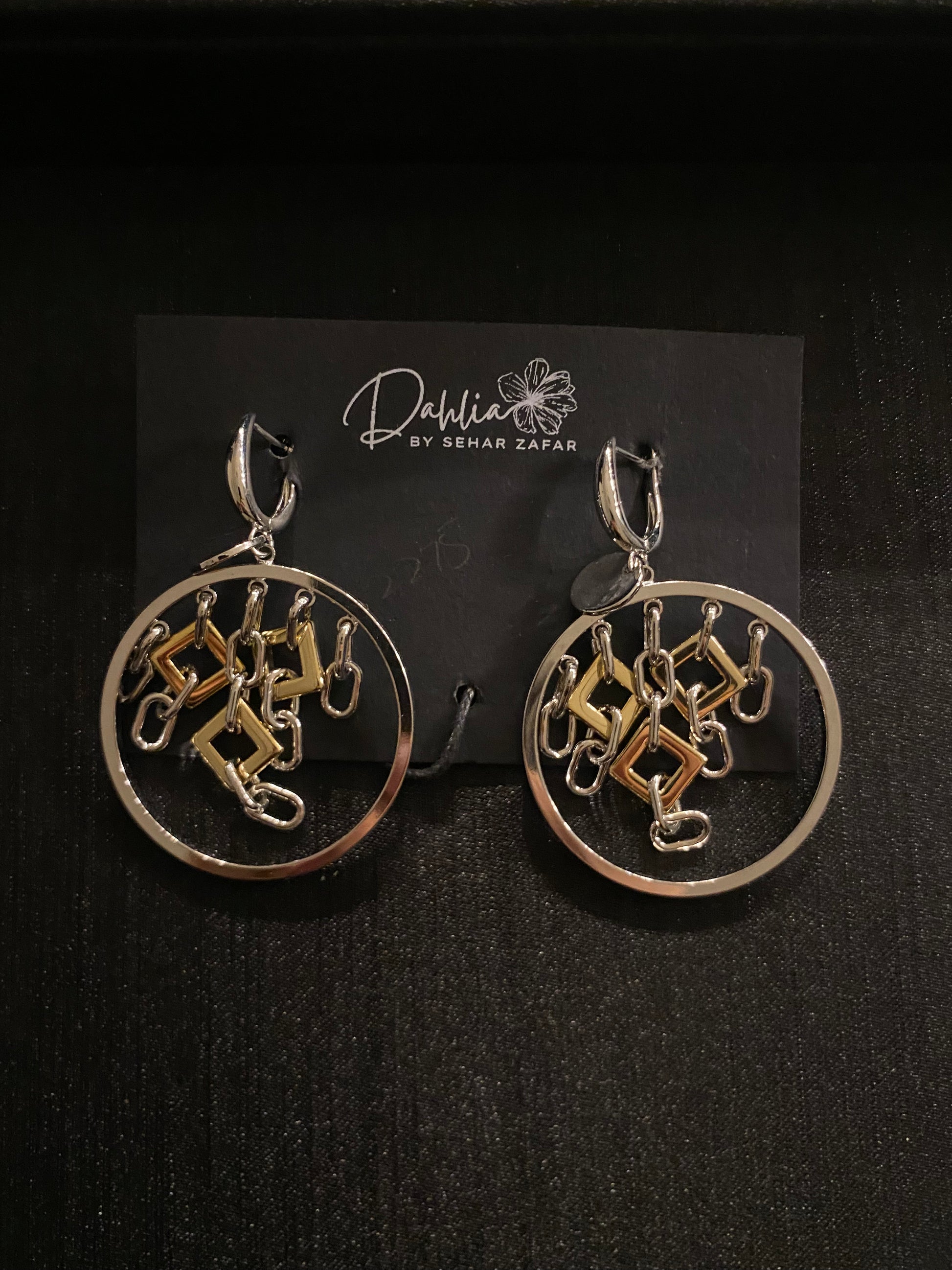 Gold circular earrings with geometric hanging elements in mixed metal on black branded card