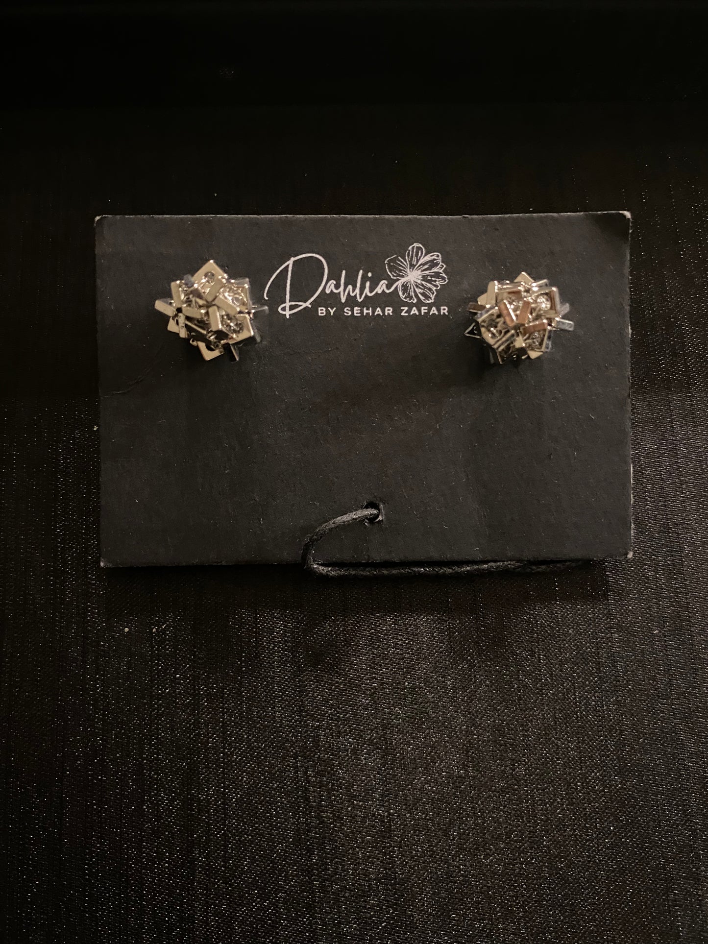 Gold geometric earrings with interlocking metallic pieces on black branded card