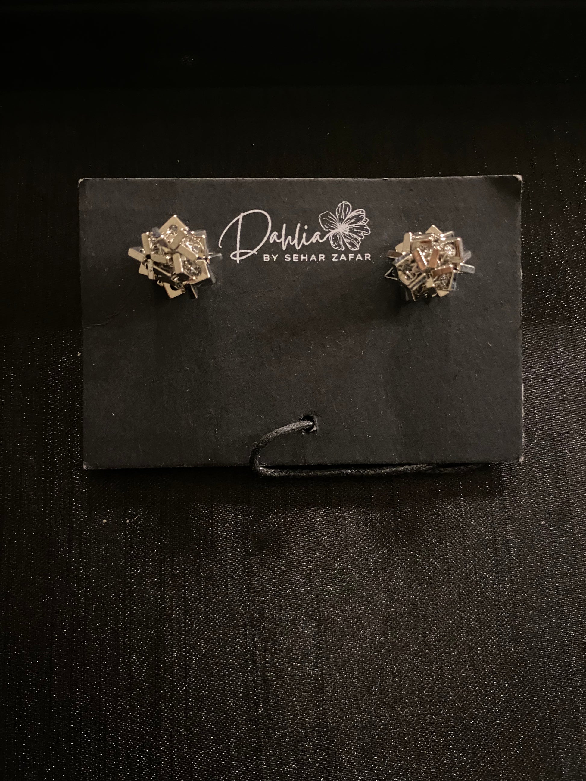 Gold geometric earrings with interlocking metallic pieces on black branded card