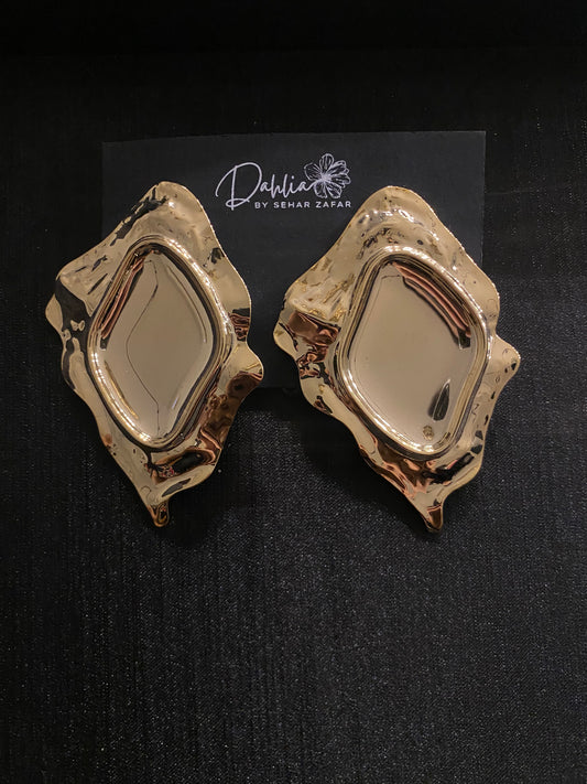 Gold abstract earrings with diamond-shaped center and molten-style frame on black branded card
