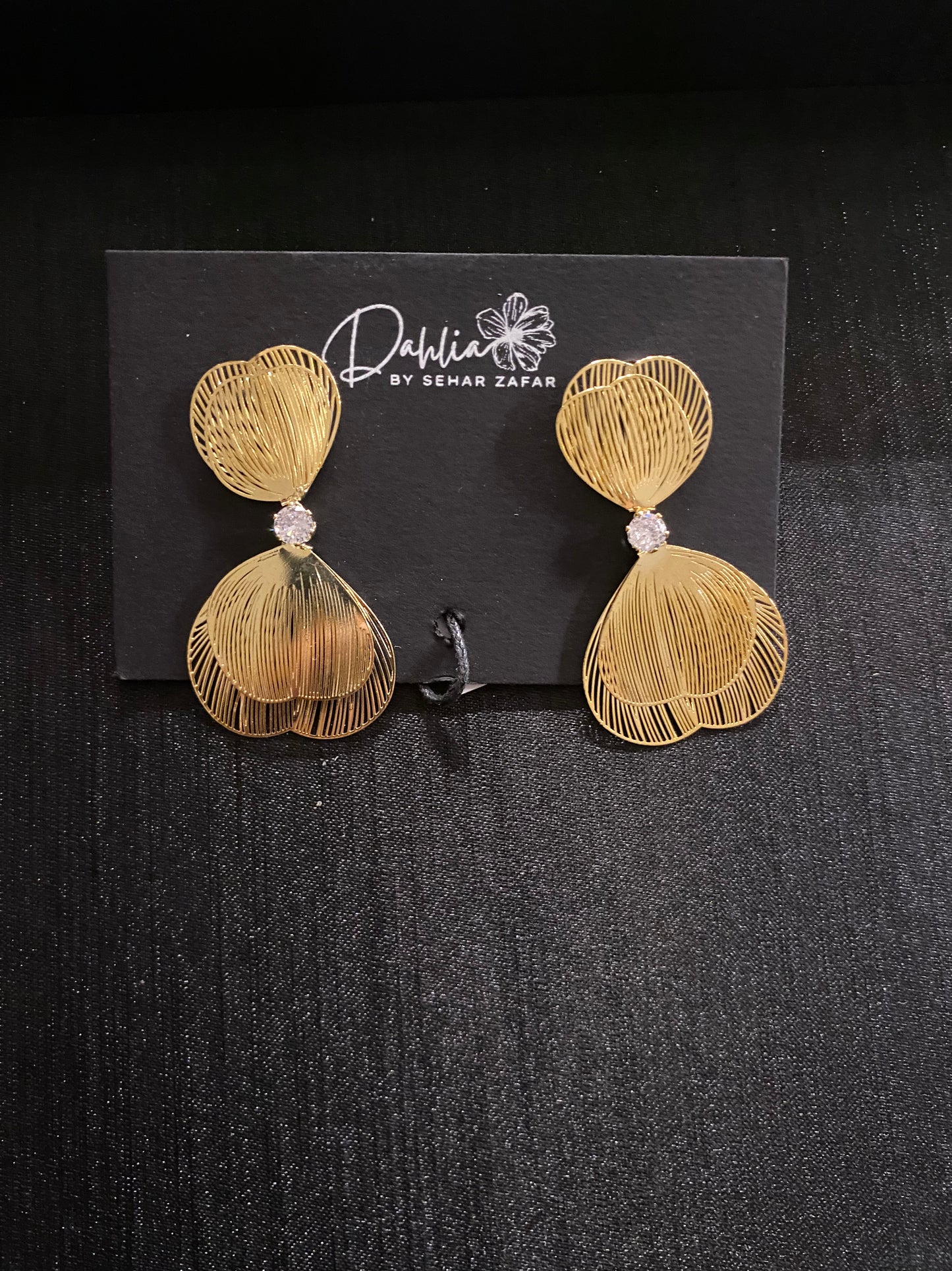 Elegant Gold Earrings displayed on a black dahlia branded card resting on a textured surface 
