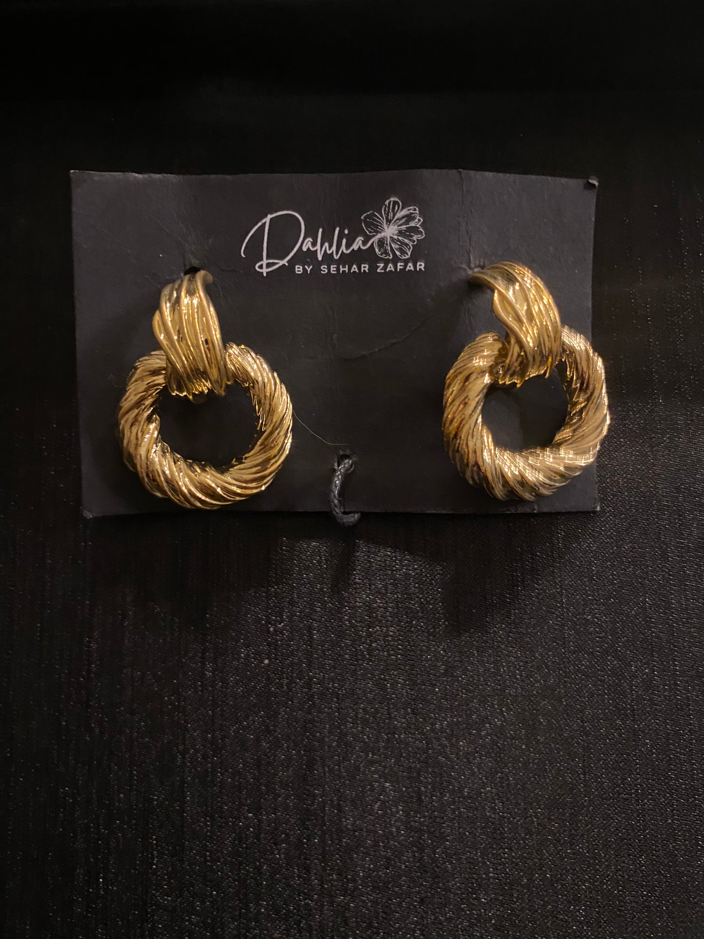 Gold twisted hoop earrings with rope texture on black branded card
