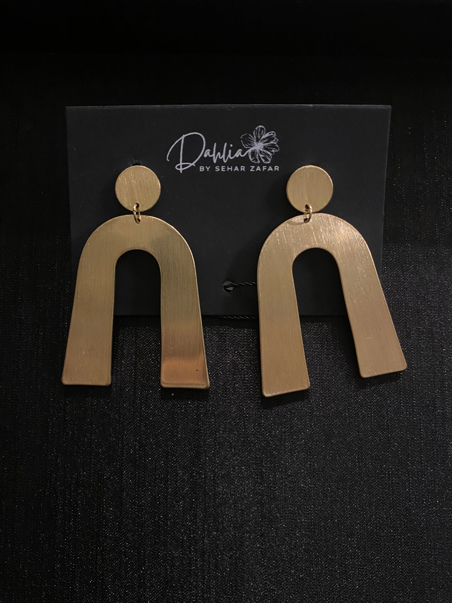 Gold geometric arch earrings with brushed texture on black branded card