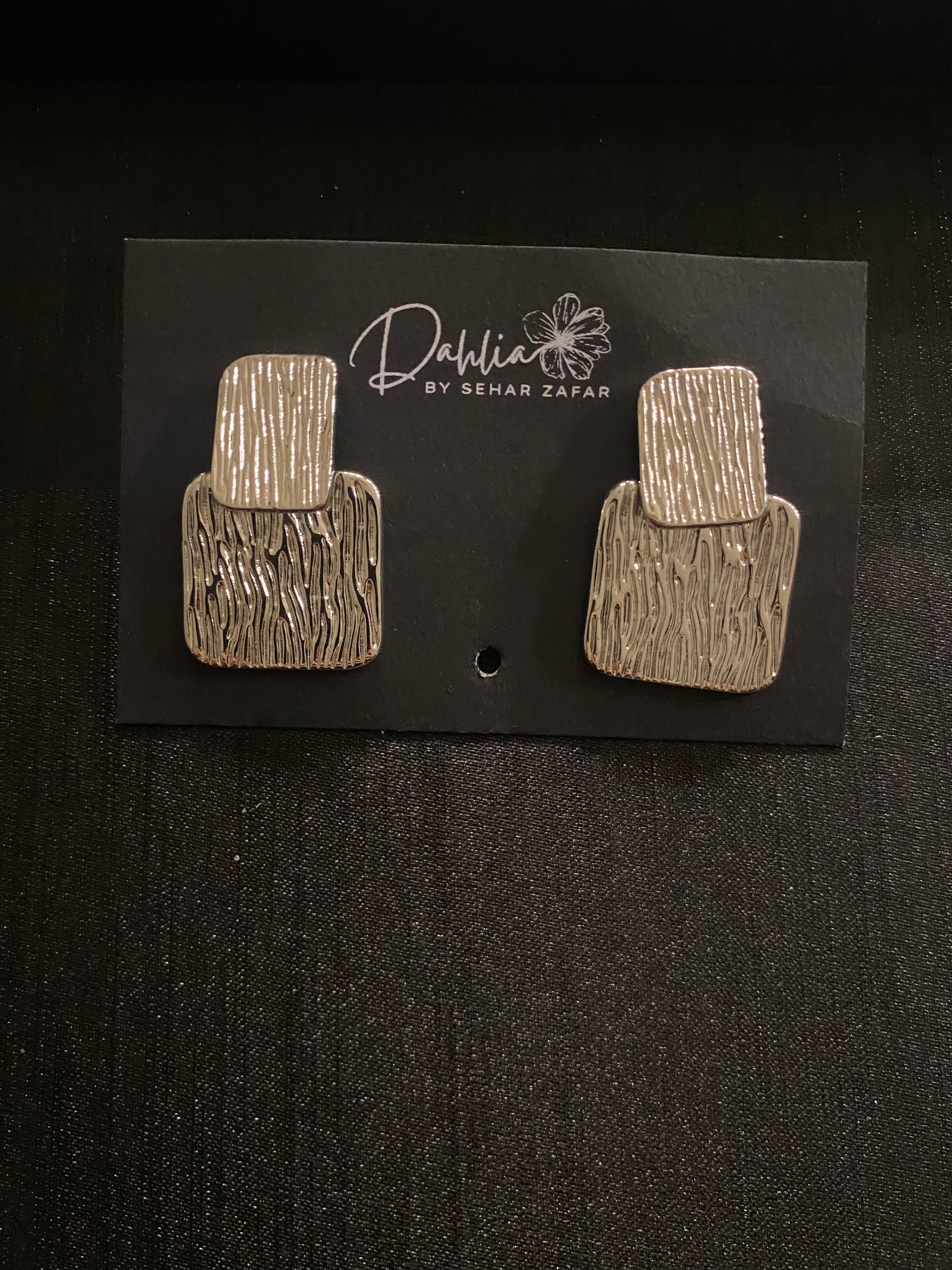 Gold rectangular earrings with vertical groove texture on black branded card