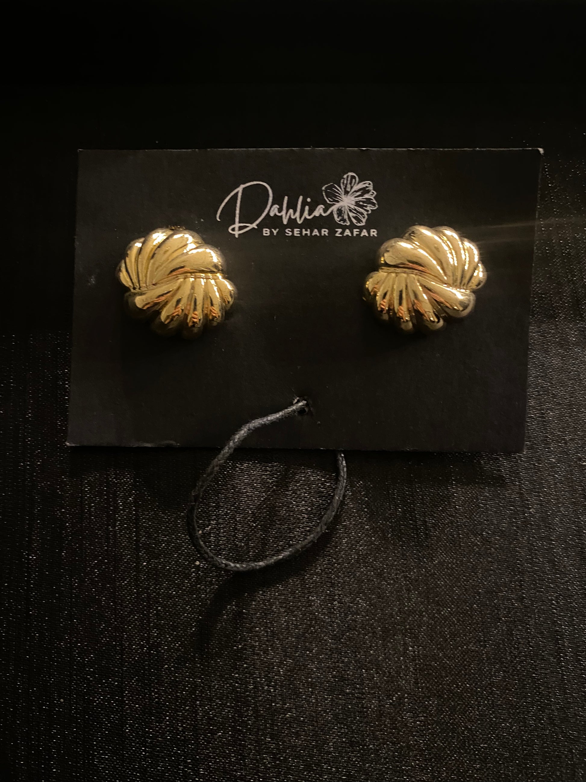 Gold shell-shaped earrings with ridged texture on black branded card