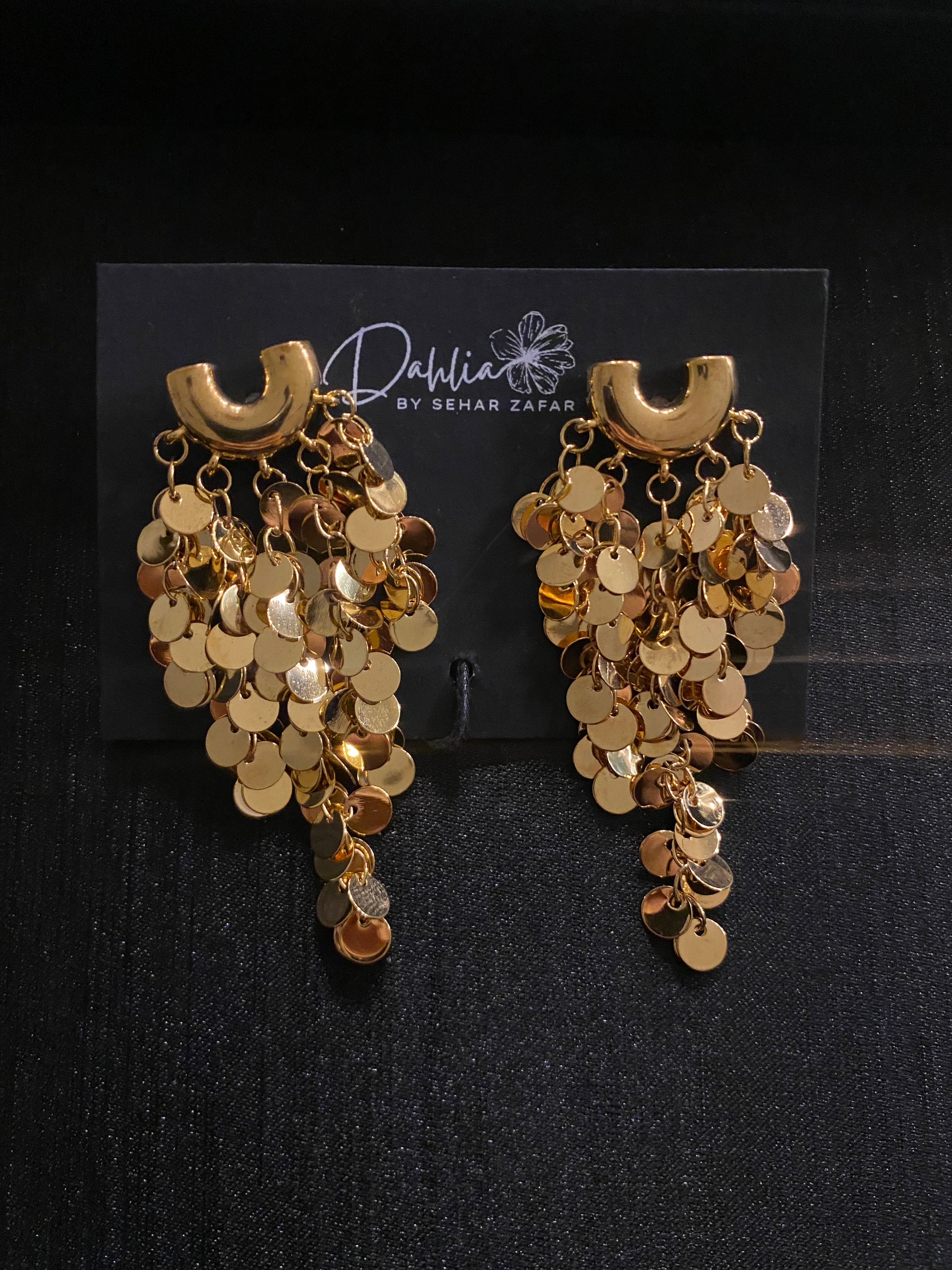 Gold cascading disc earrings with curved top accent on black branded card