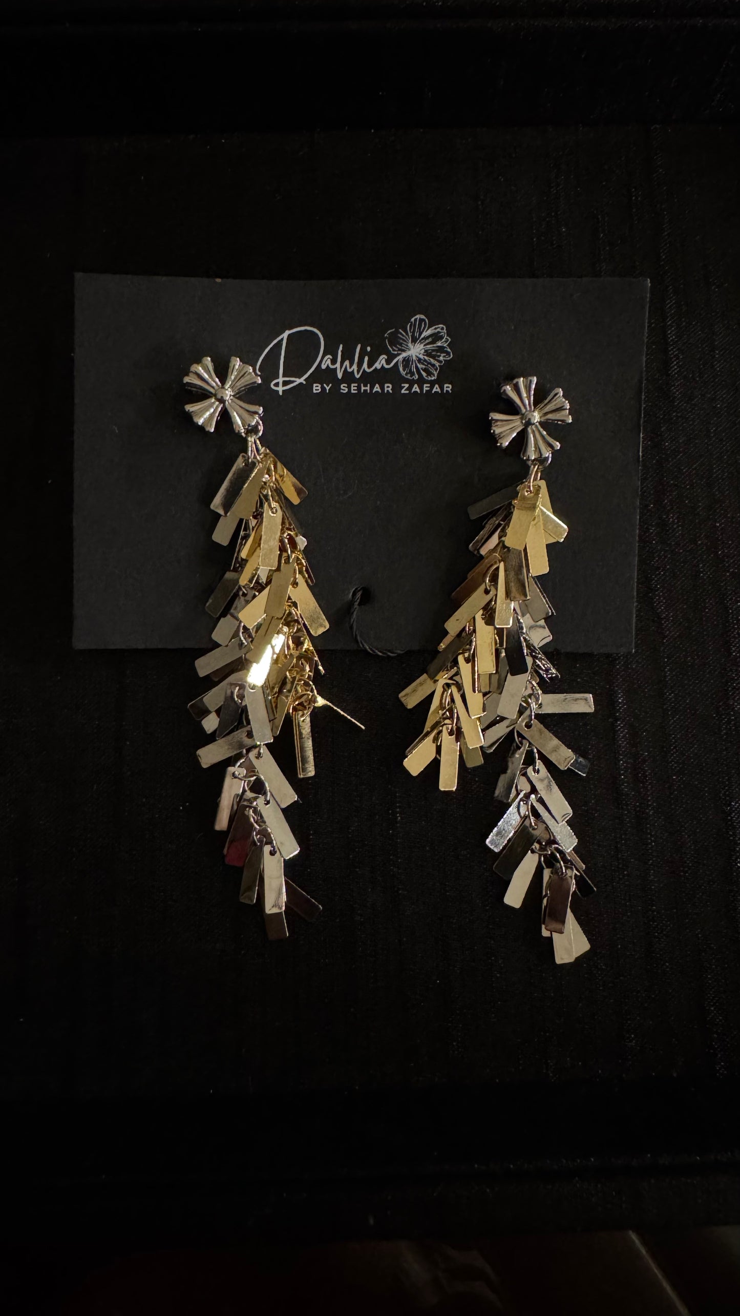 Gold and silver cascading earrings with floral stud and geometric drops on black branded card