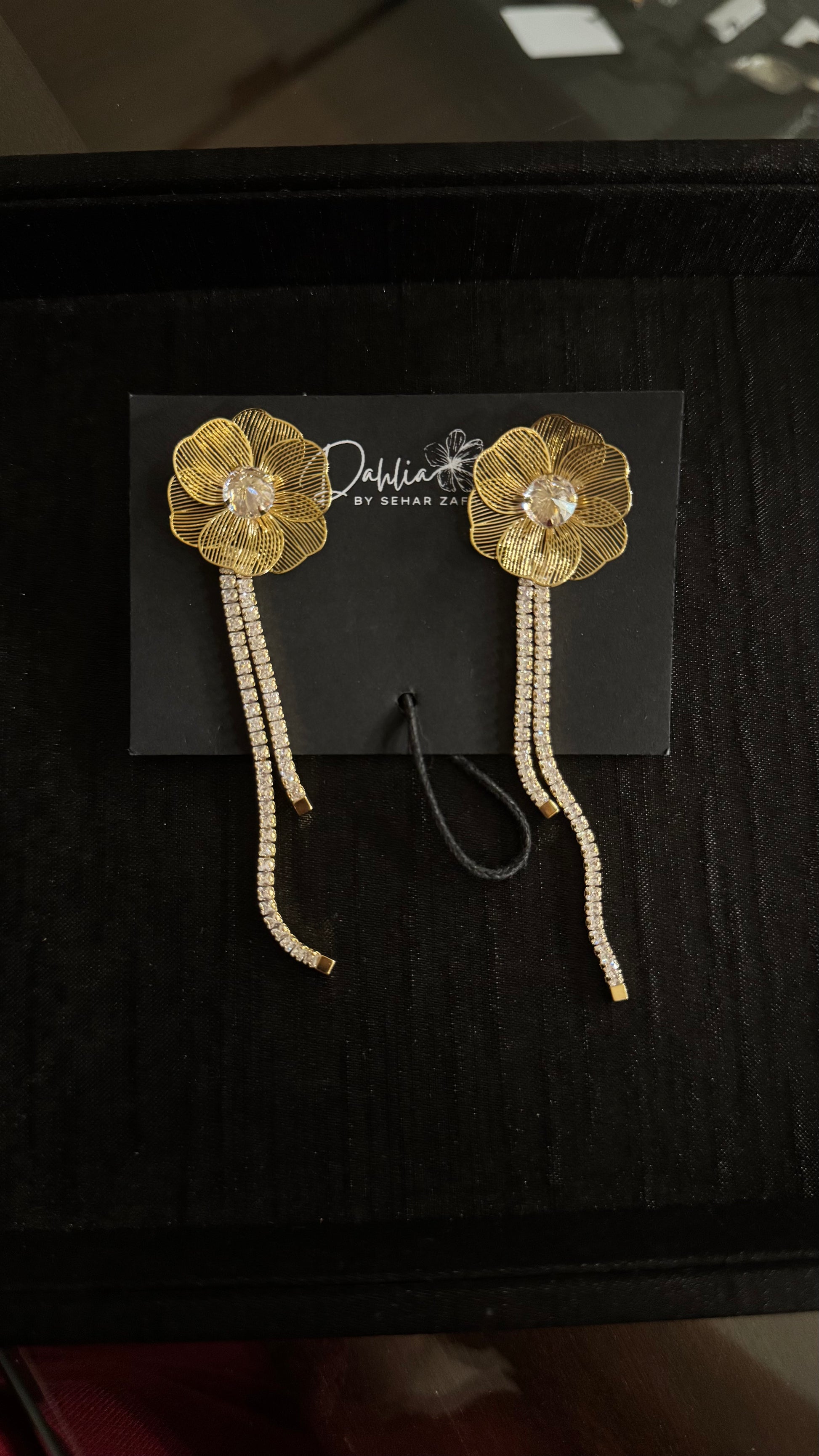 Gold floral earrings with crystal drops and petal detailing on black branded card