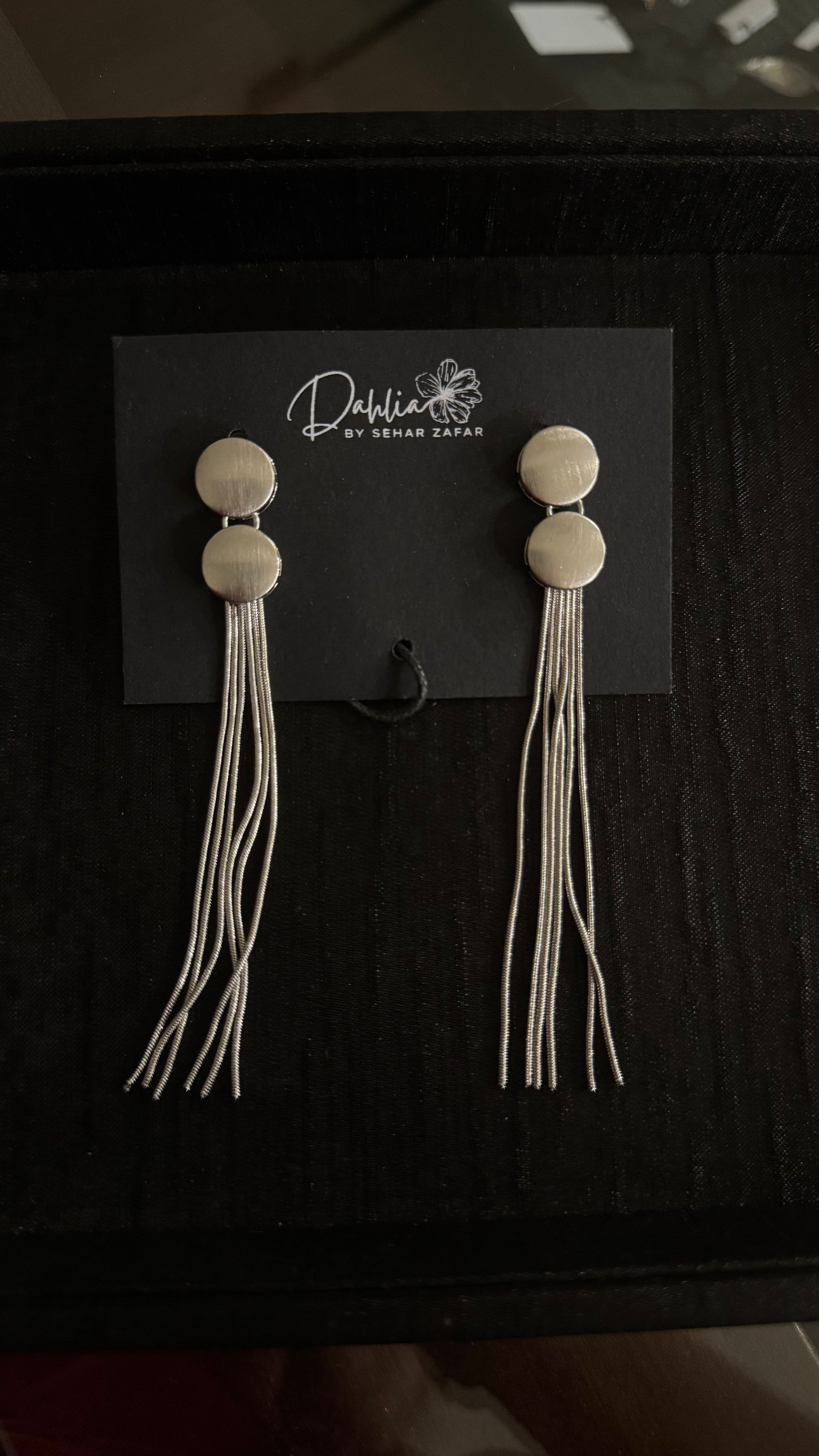 Gold double disc earrings with flowing thread-like strands on black branded card