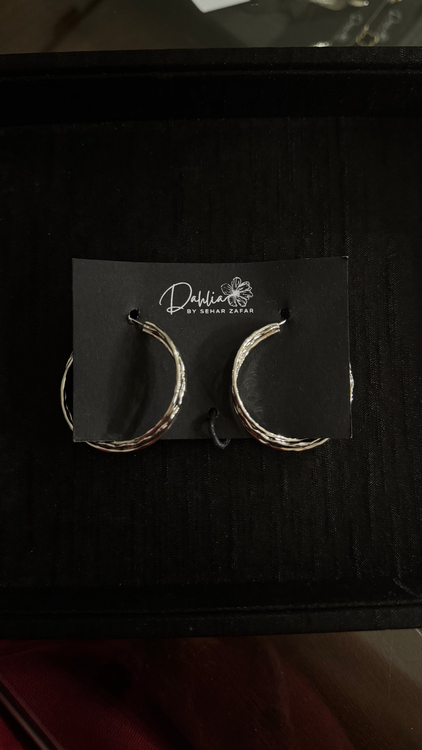 Silver twisted hoop earrings with textured finish on black branded card