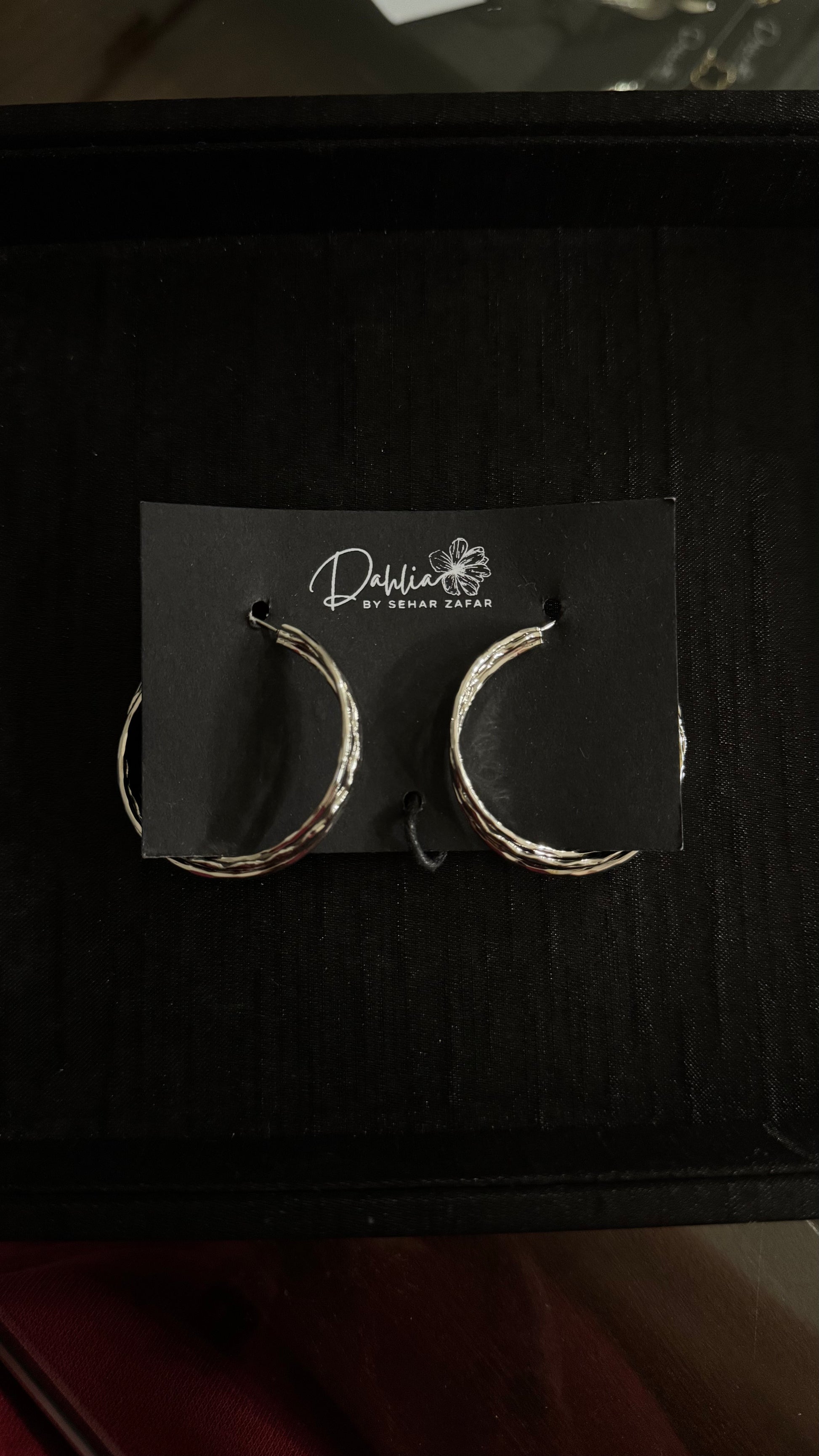 Silver twisted hoop earrings with textured finish on black branded card