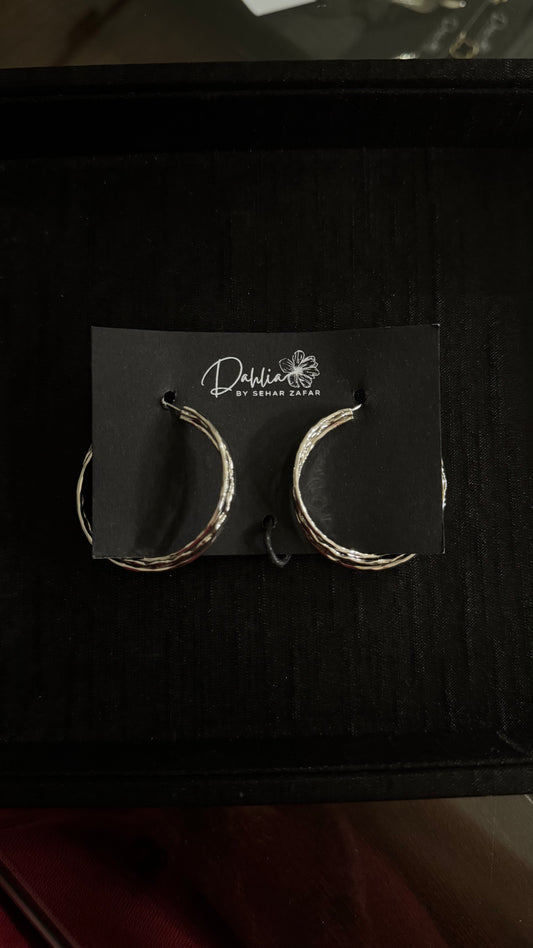 Silver twisted hoop earrings with textured finish on black branded card