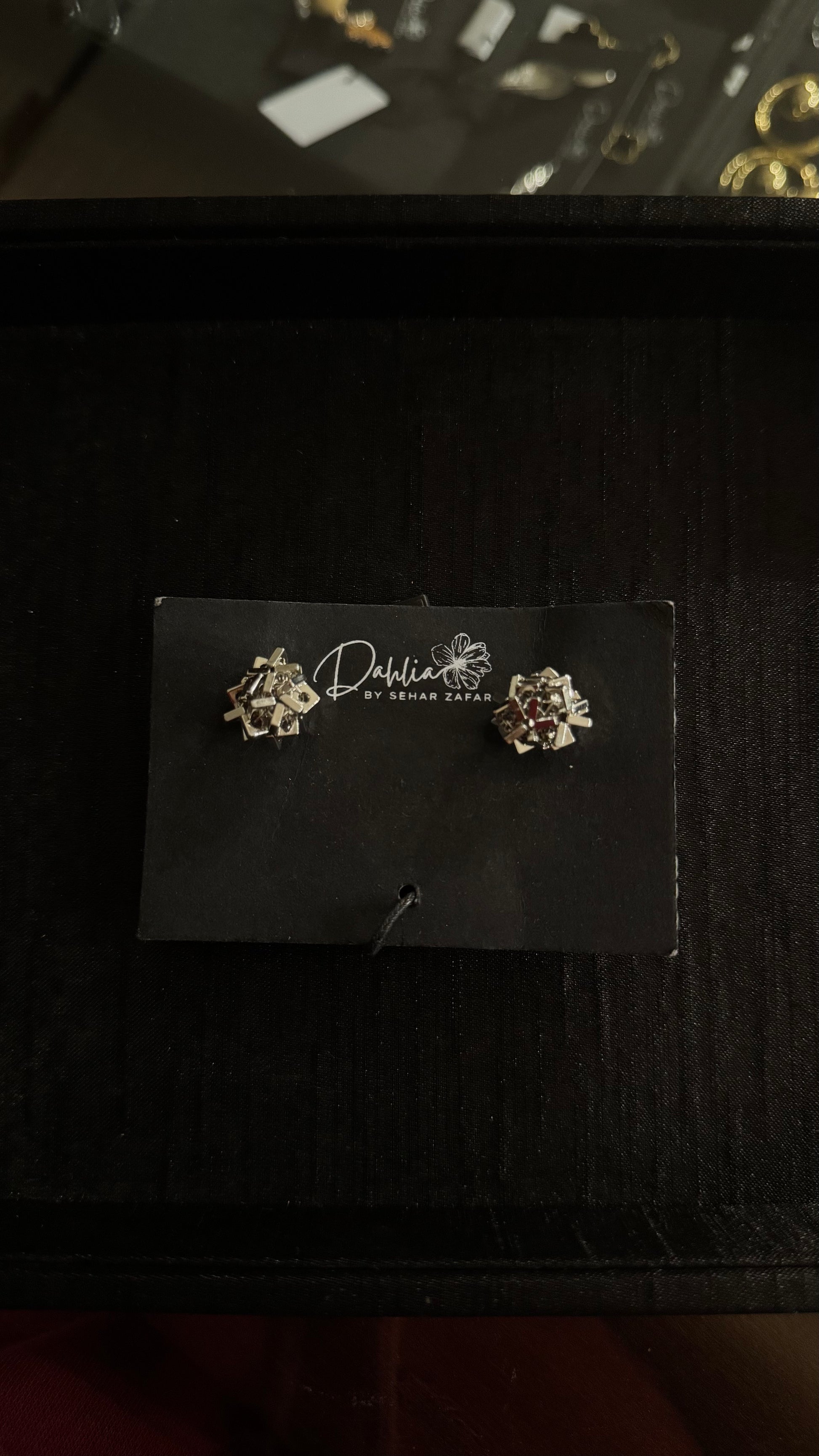 Gold floral earrings with crystal accents and ornate detailing on black branded card