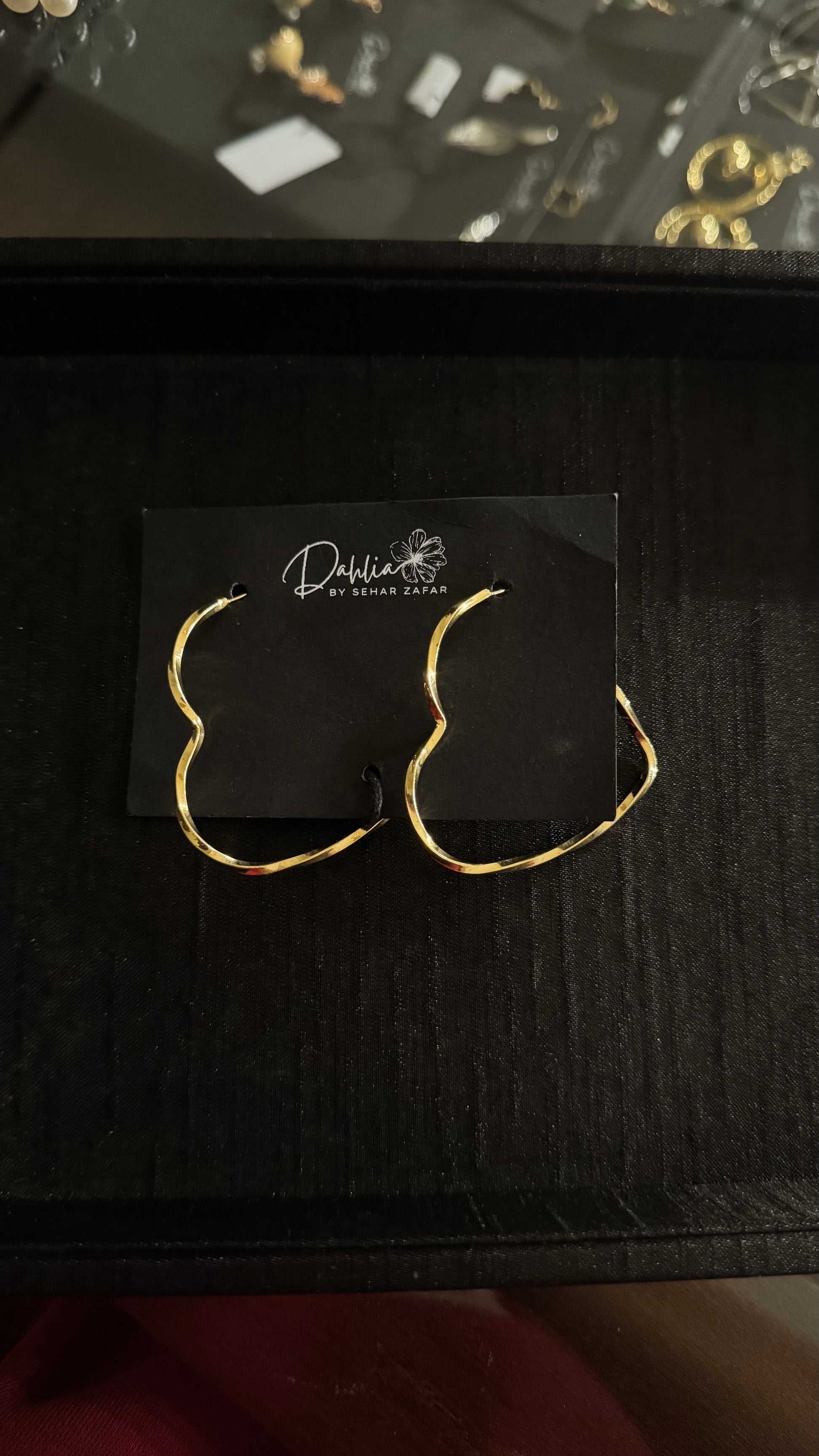 Gold wavy hoop earrings with irregular sculptural design on black branded card