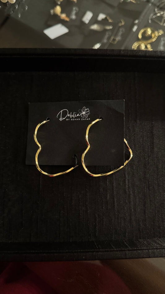 Gold wavy hoop earrings with irregular sculptural design on black branded card