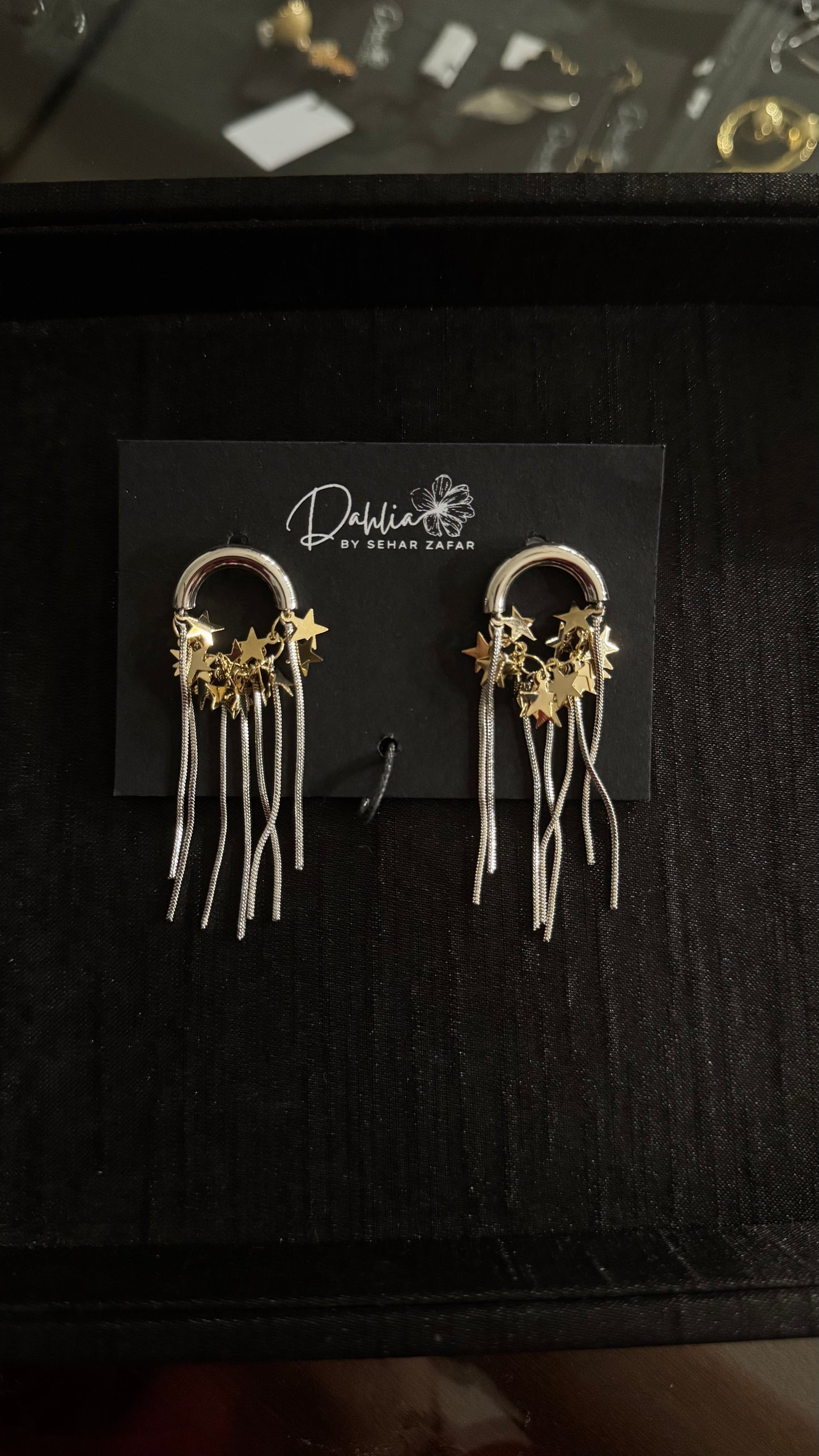 Silver and gold celestial earrings with arch frame and dangling star and moon charms on black branded card