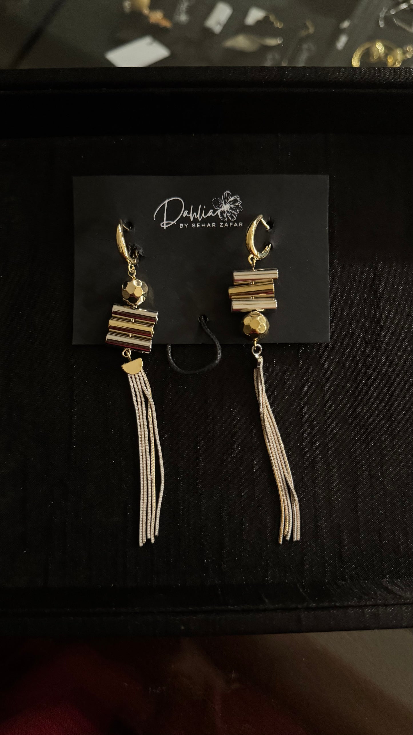 Gold hoop tassel earrings with faceted bead and geometric stack on black branded card