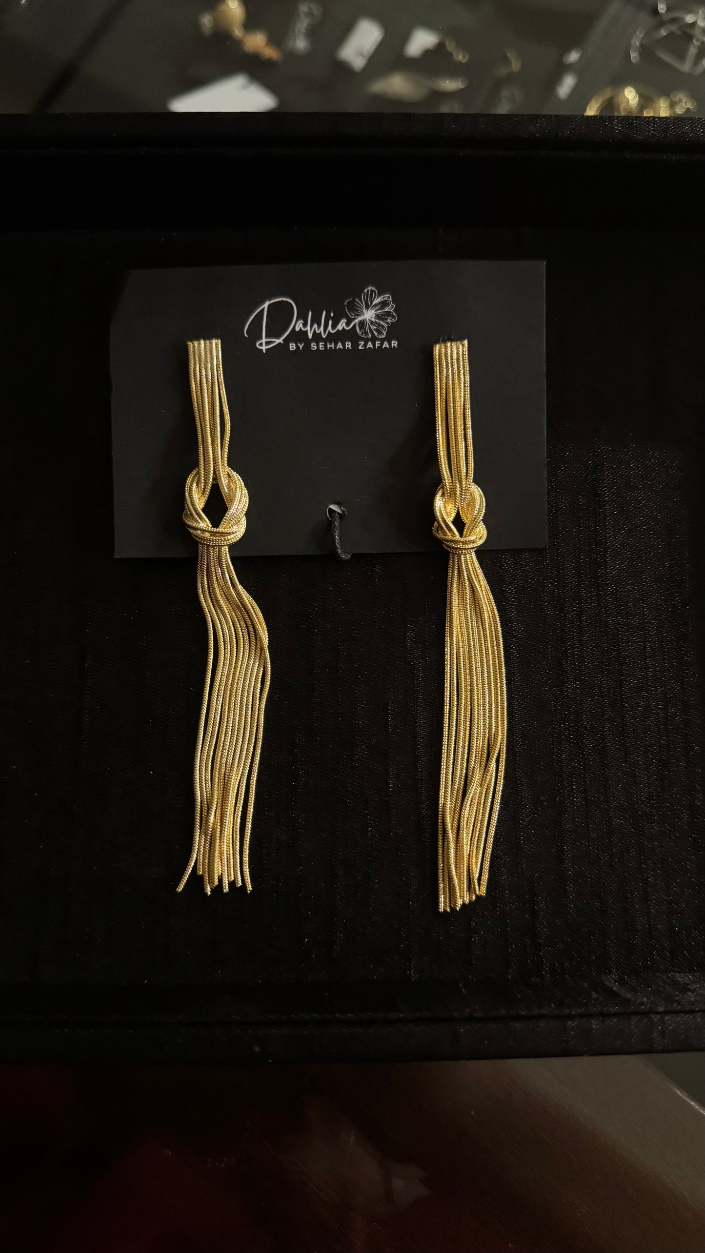 Gold tassel earrings with knotted top and flowing strands on black branded card