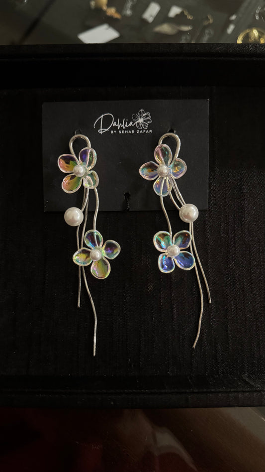 Iridescent floral earrings with pearl accents and curved metallic strands on black branded card