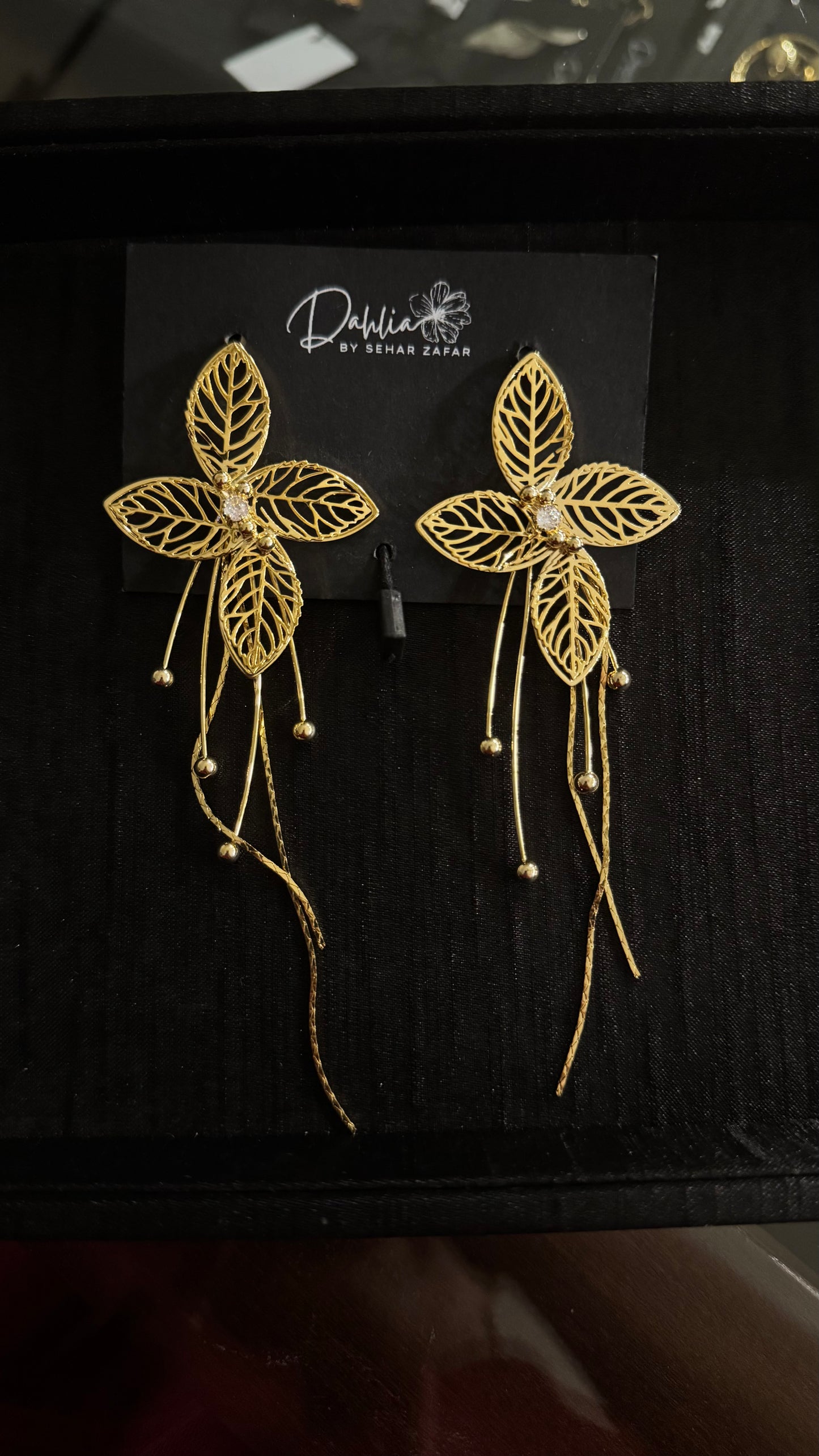 Gold filigree floral earrings with beaded tassel strands on black branded card