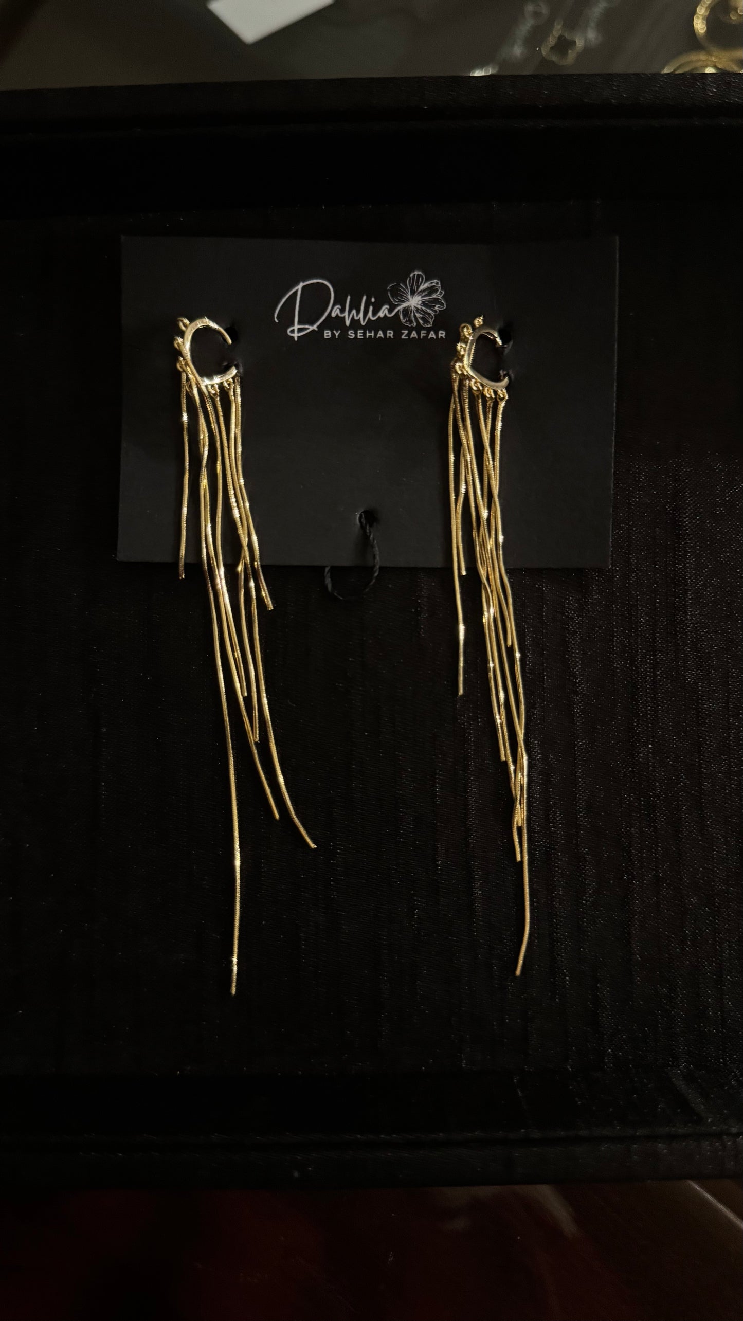 Gold hoop earrings with cascading metallic strands on black branded card