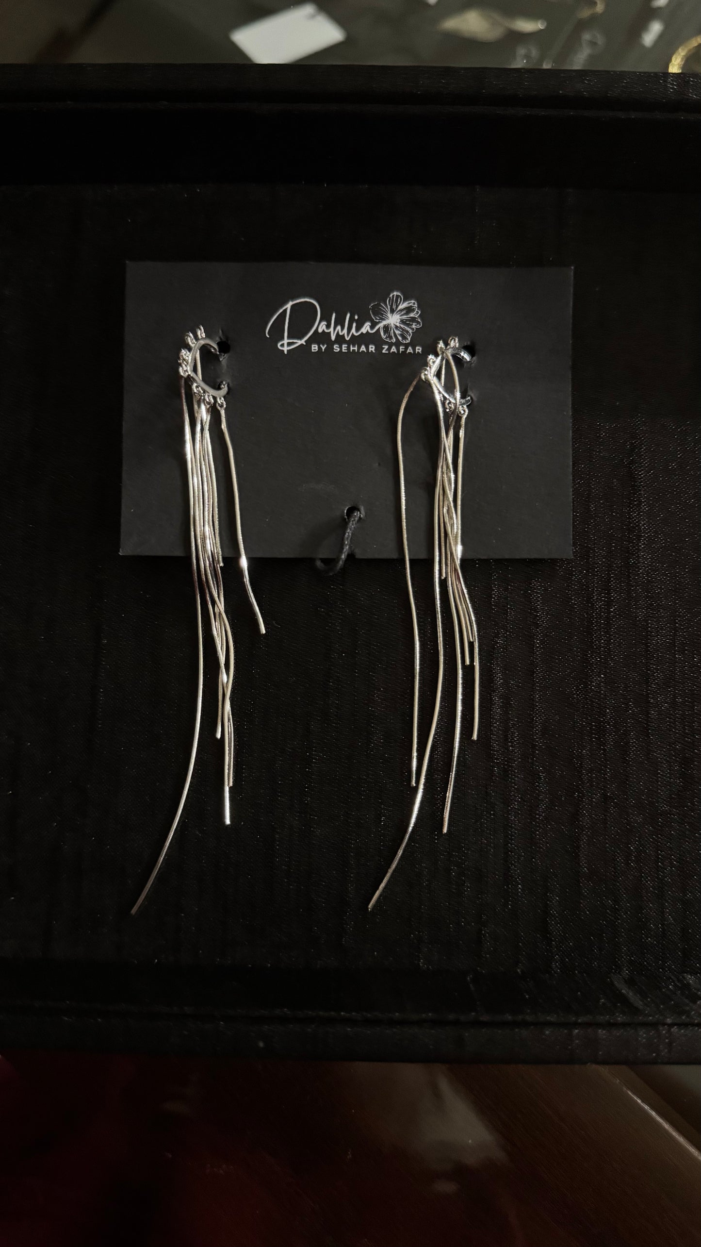 Gold hoop earrings with cascading metallic strands on black branded card