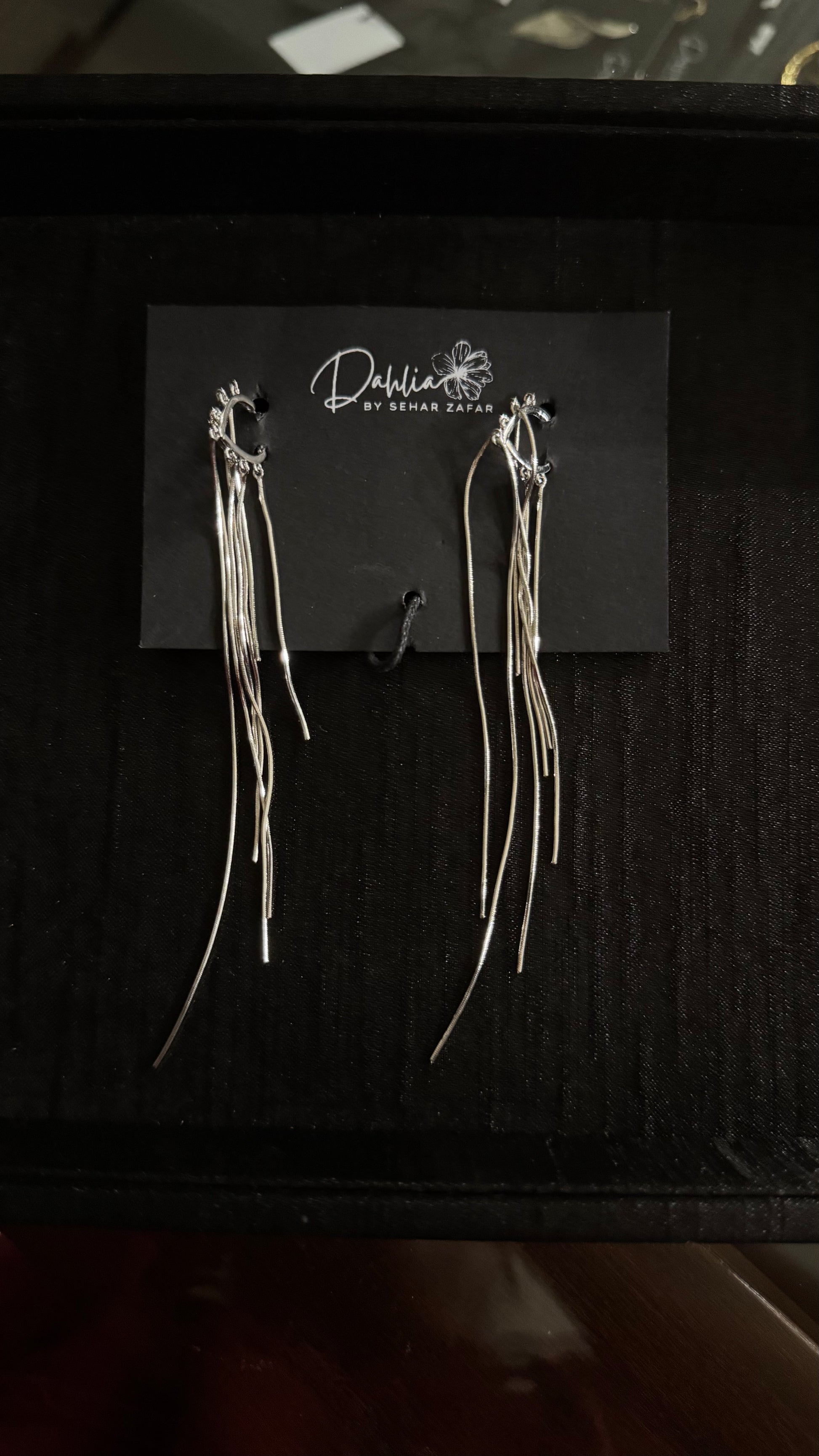 Gold hoop earrings with cascading metallic strands on black branded card