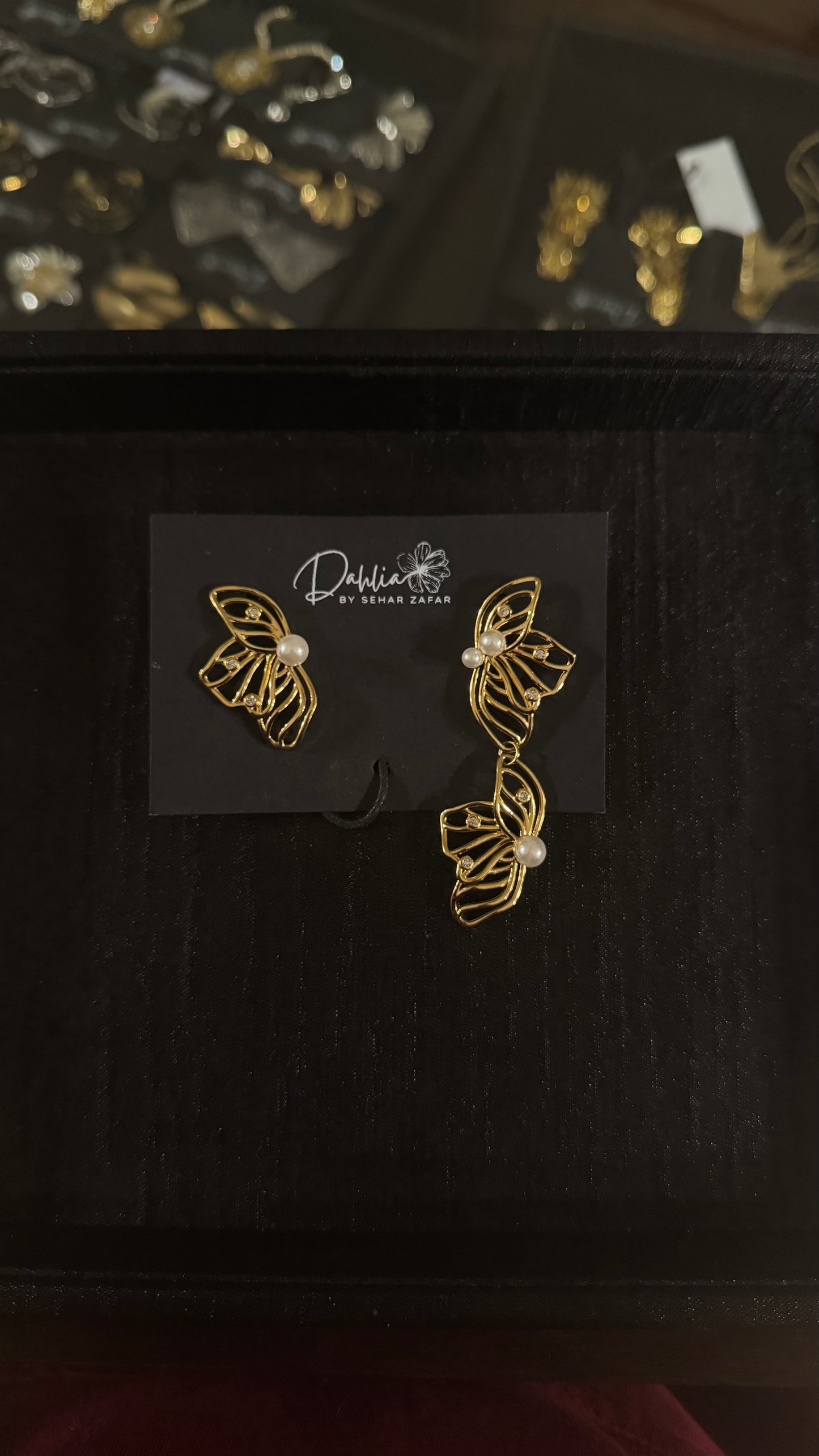 Asymmetrical gold wire earrings with pearl accents and artistic floral design on black branded card