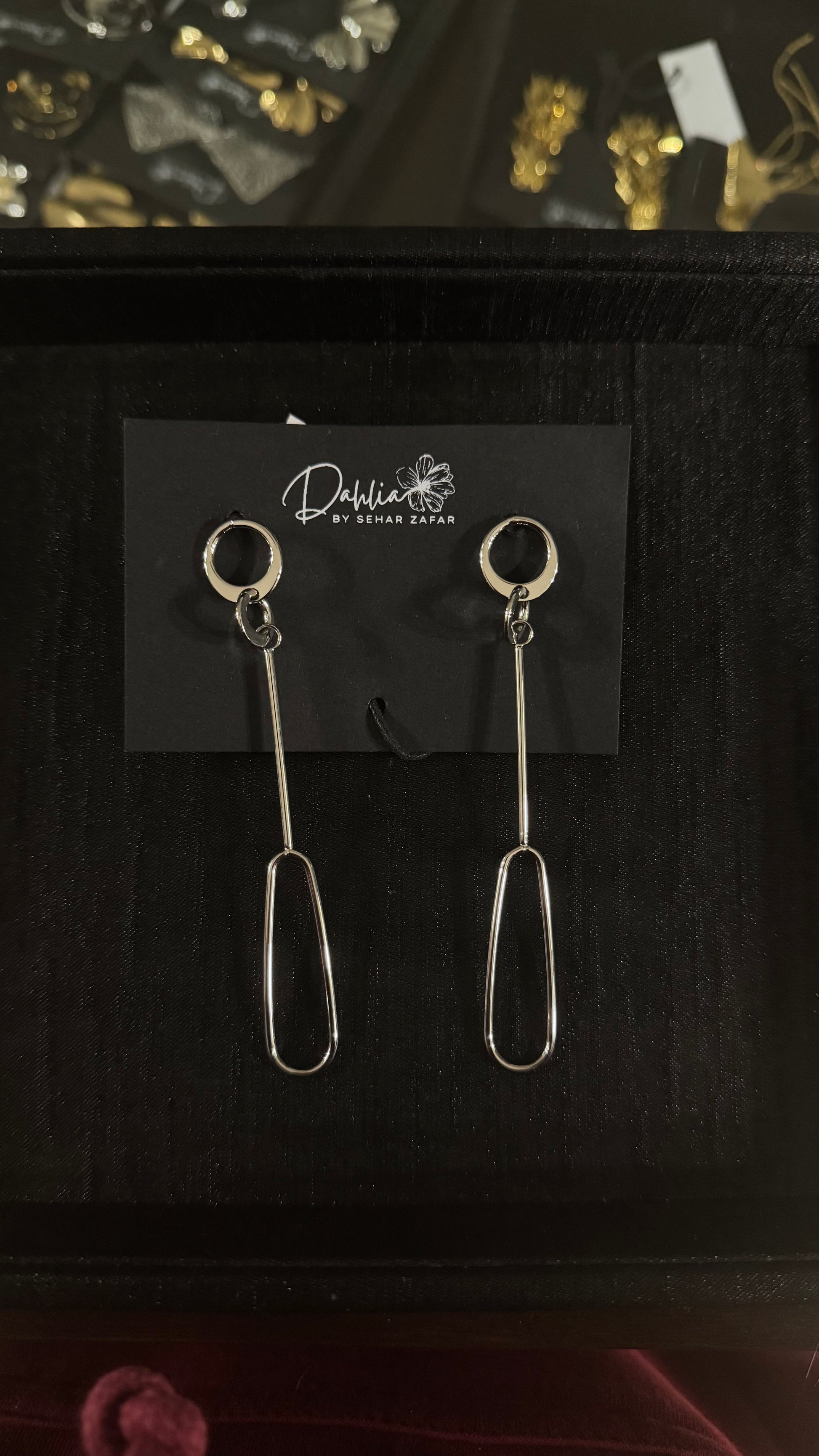 Gold minimalist oval loop earrings with vertical bar drop on black branded card