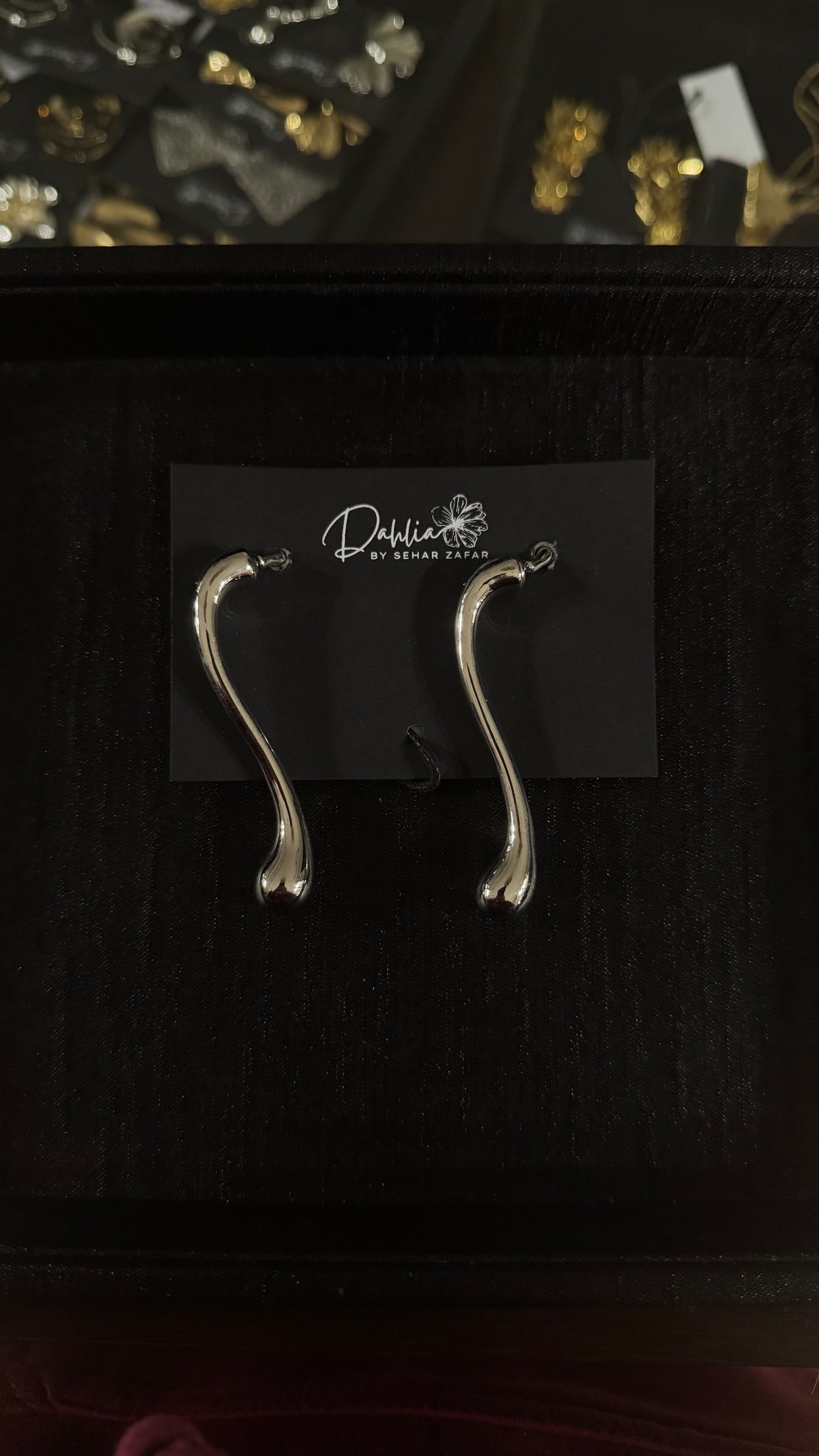 Gold abstract wishbone earrings with elongated organic curve on black branded card