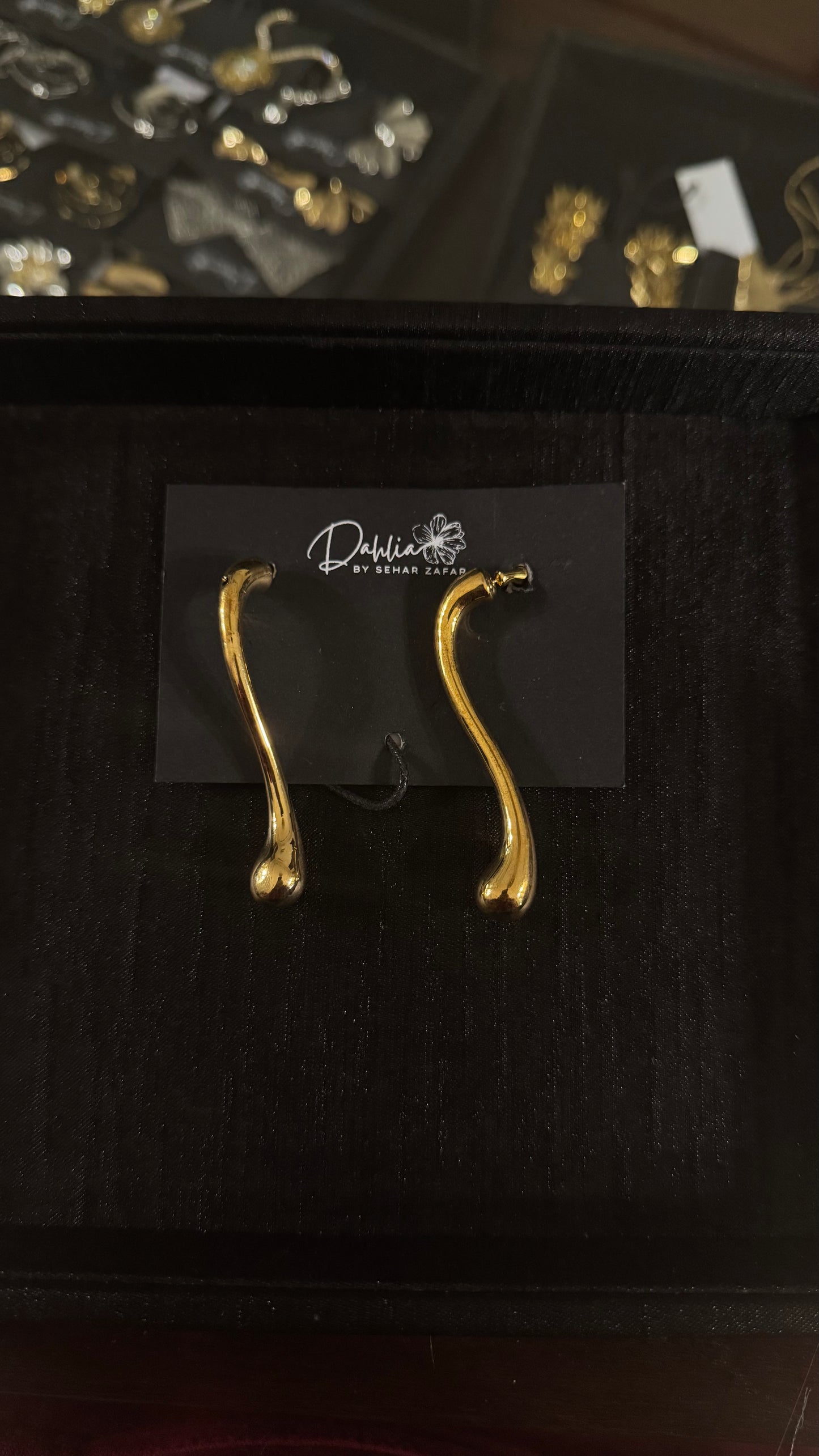 Gold abstract wishbone earrings with elongated organic curve on black branded card