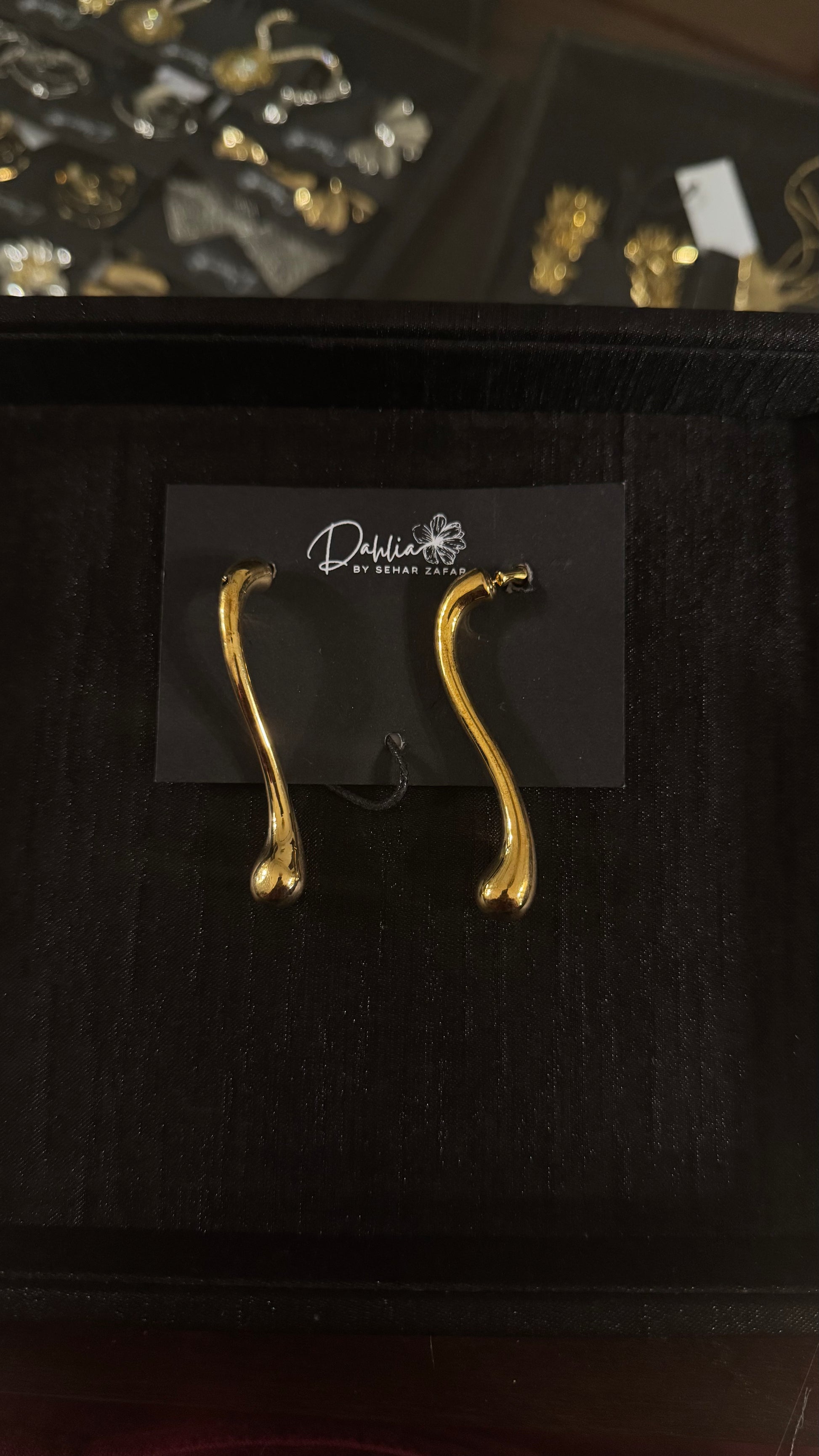 Gold abstract wishbone earrings with elongated organic curve on black branded card
