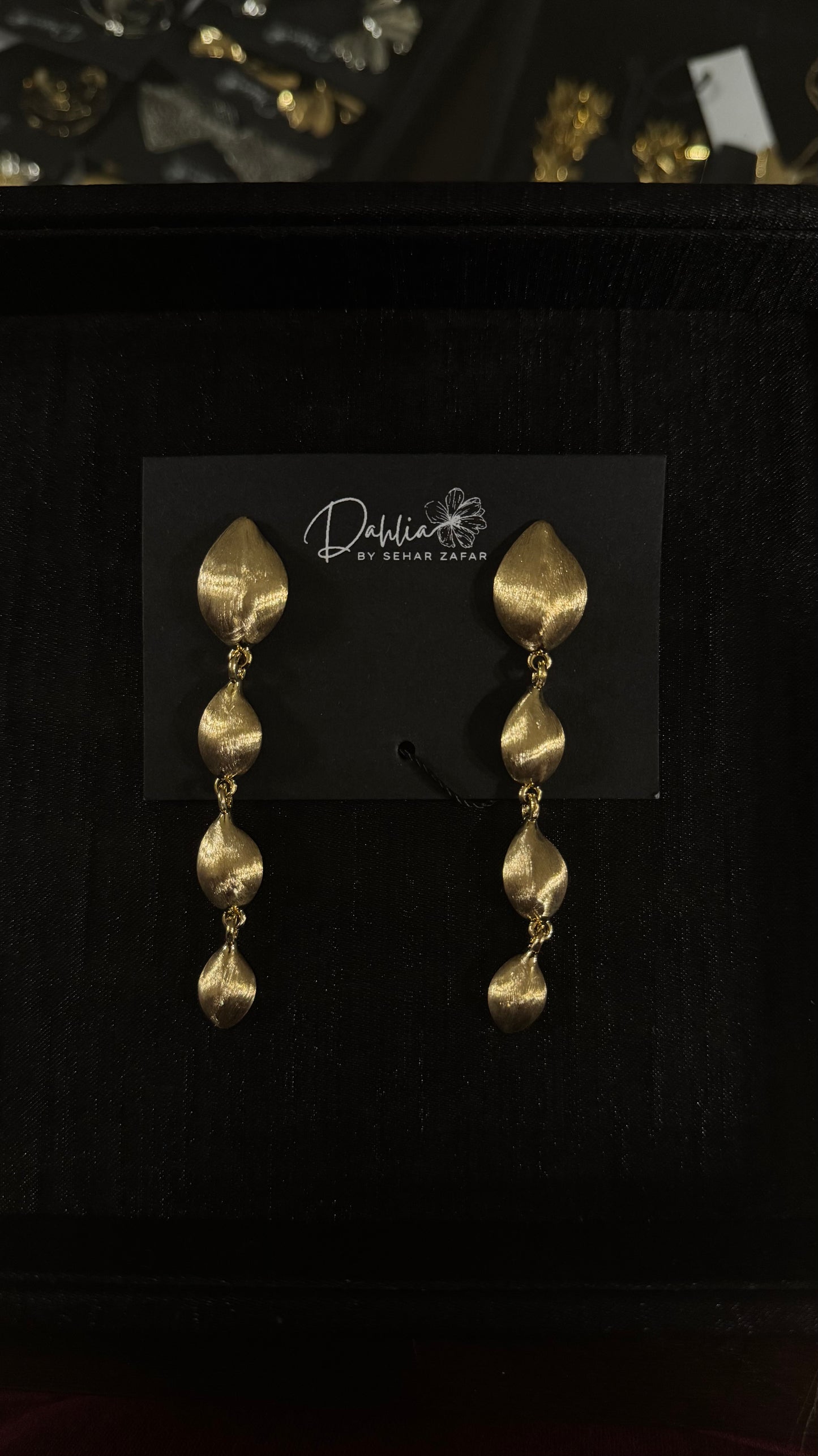 Gold cascading leaf earrings with textured metallic finish on black branded card
