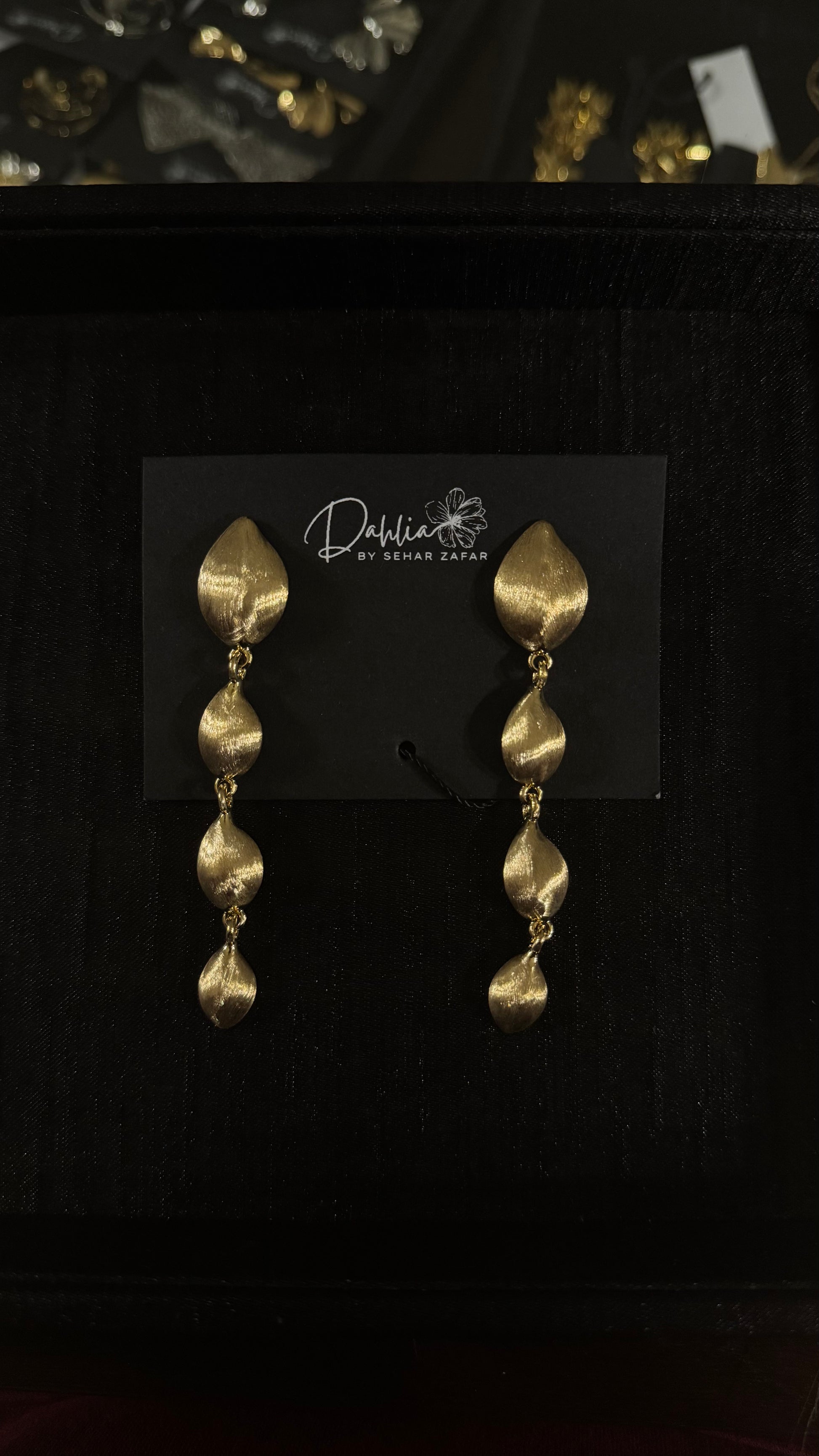 Gold cascading leaf earrings with textured metallic finish on black branded card